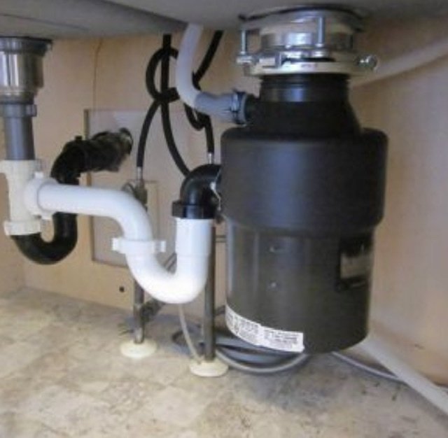 Close-up view of a kitchen sink with a garbage disposal and plumbing pipes