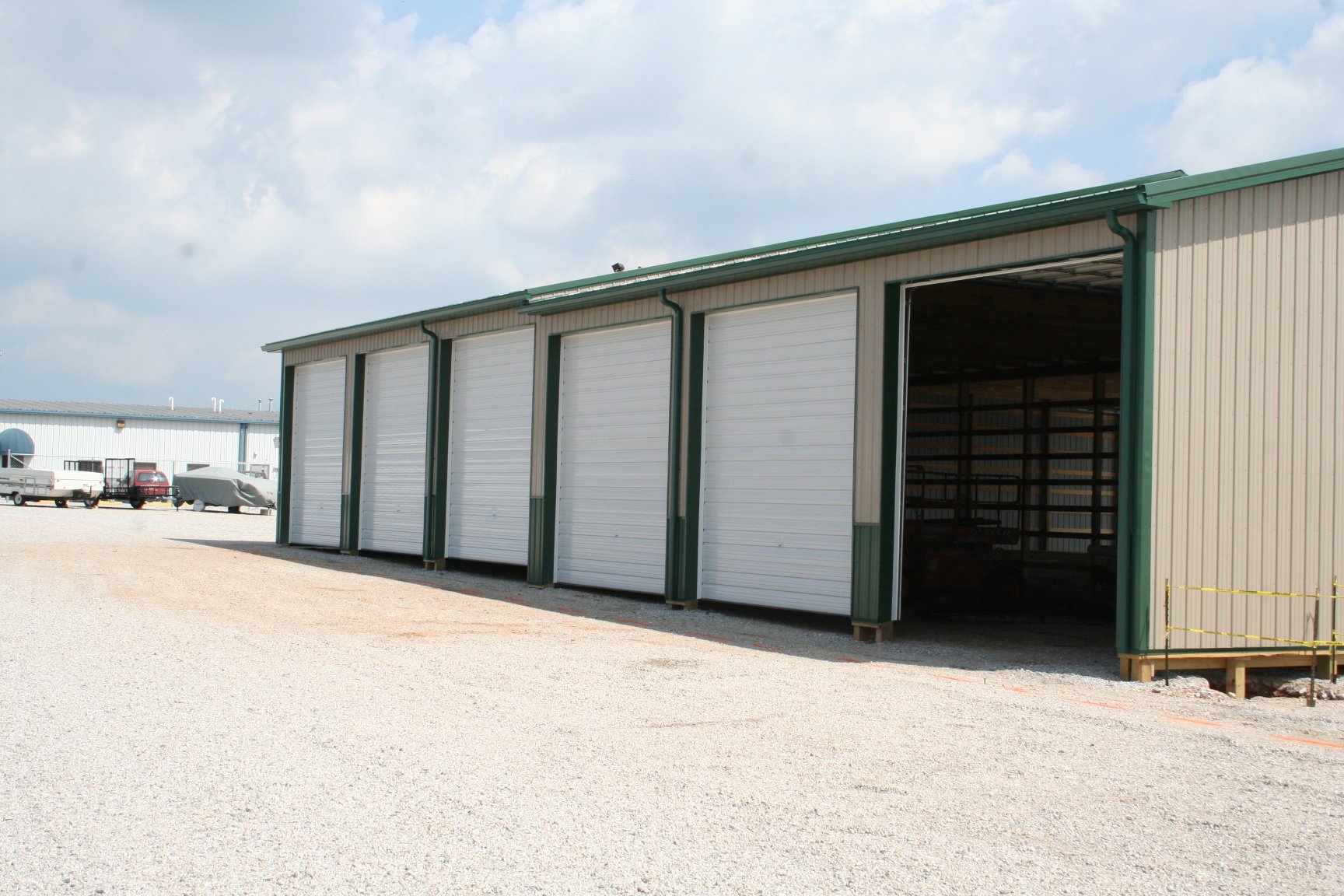 A large storage facility with multiple white roll-up doors and a green roof, under a cloudy sky