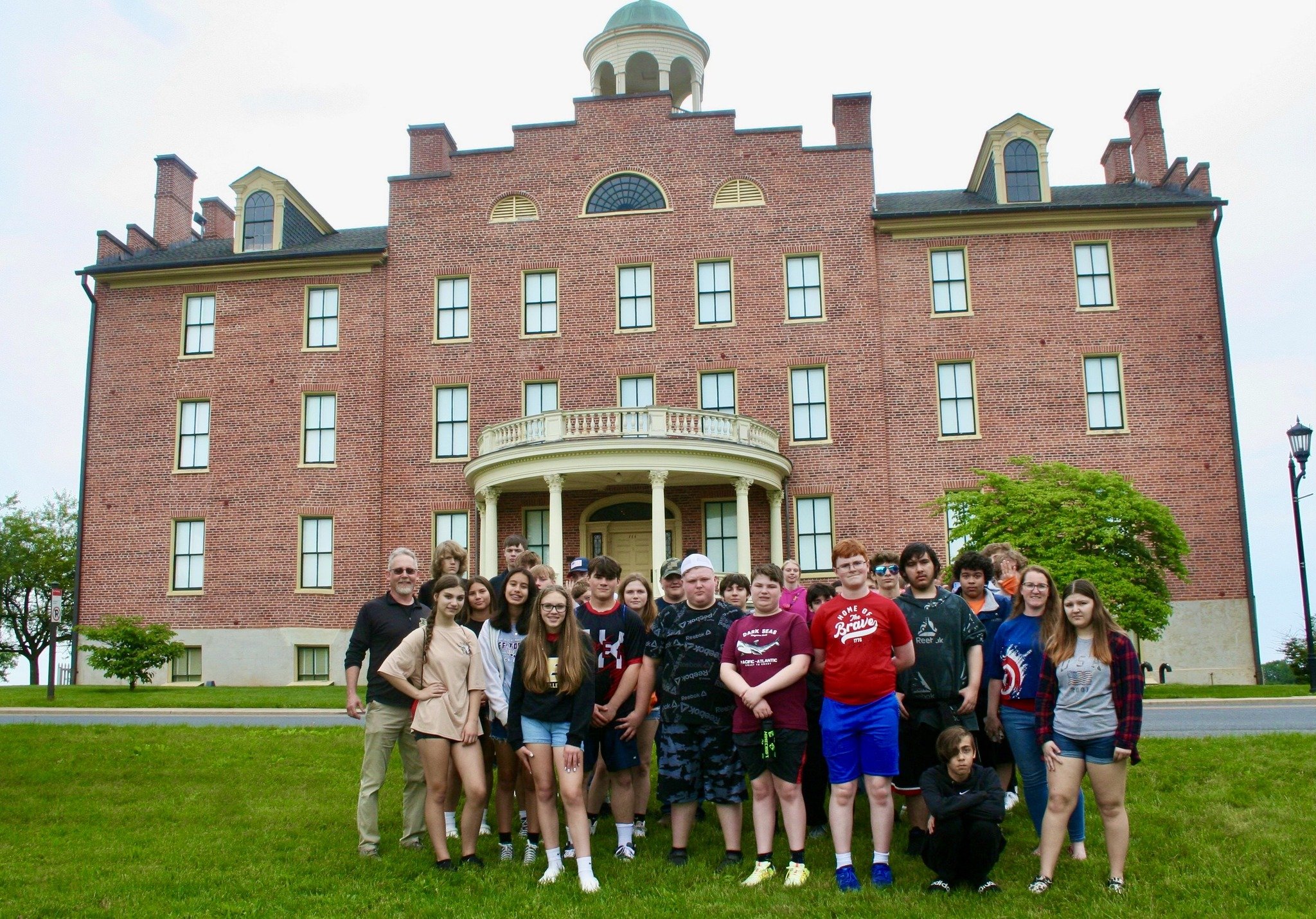 A group of students and teachers standing in front of a historic brick building.