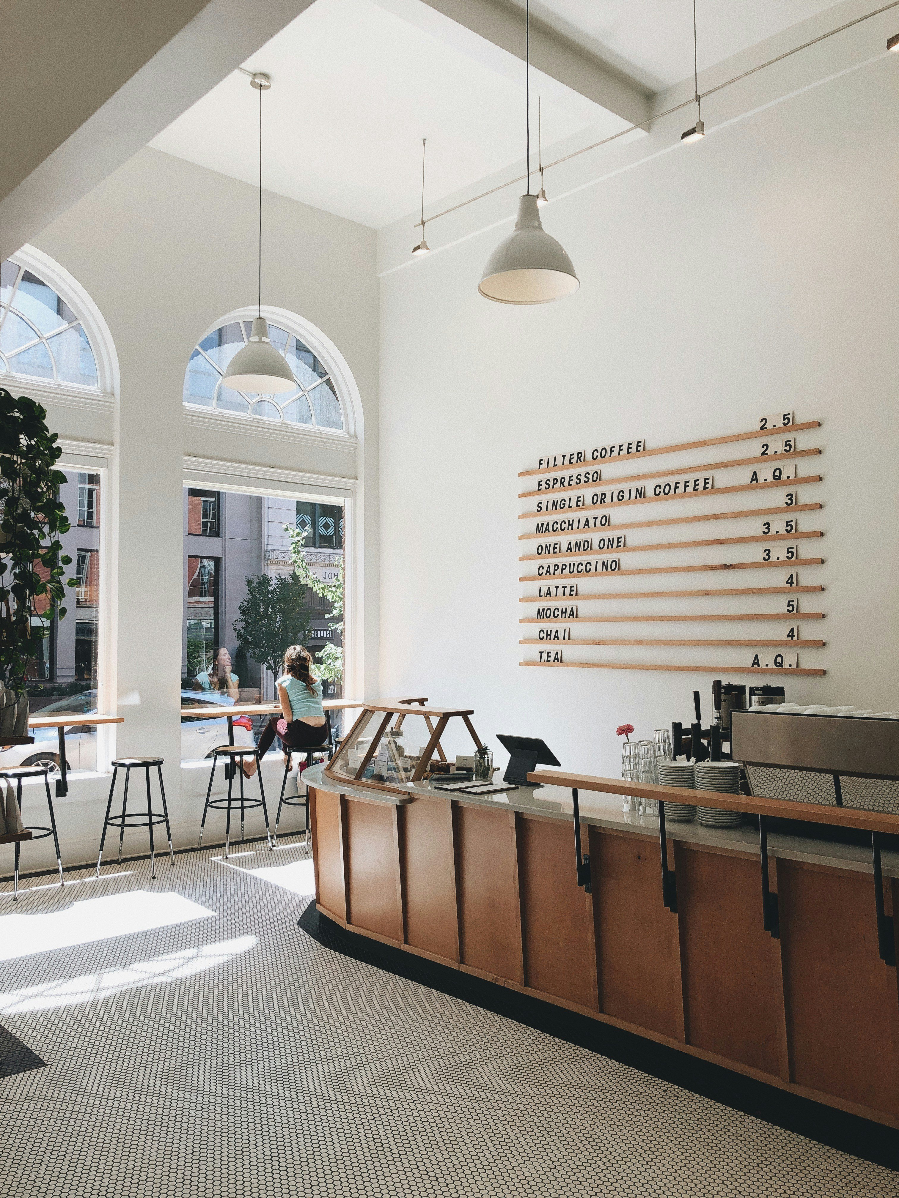 A coffee shop interior with a menu board and a woman sitting at a table.