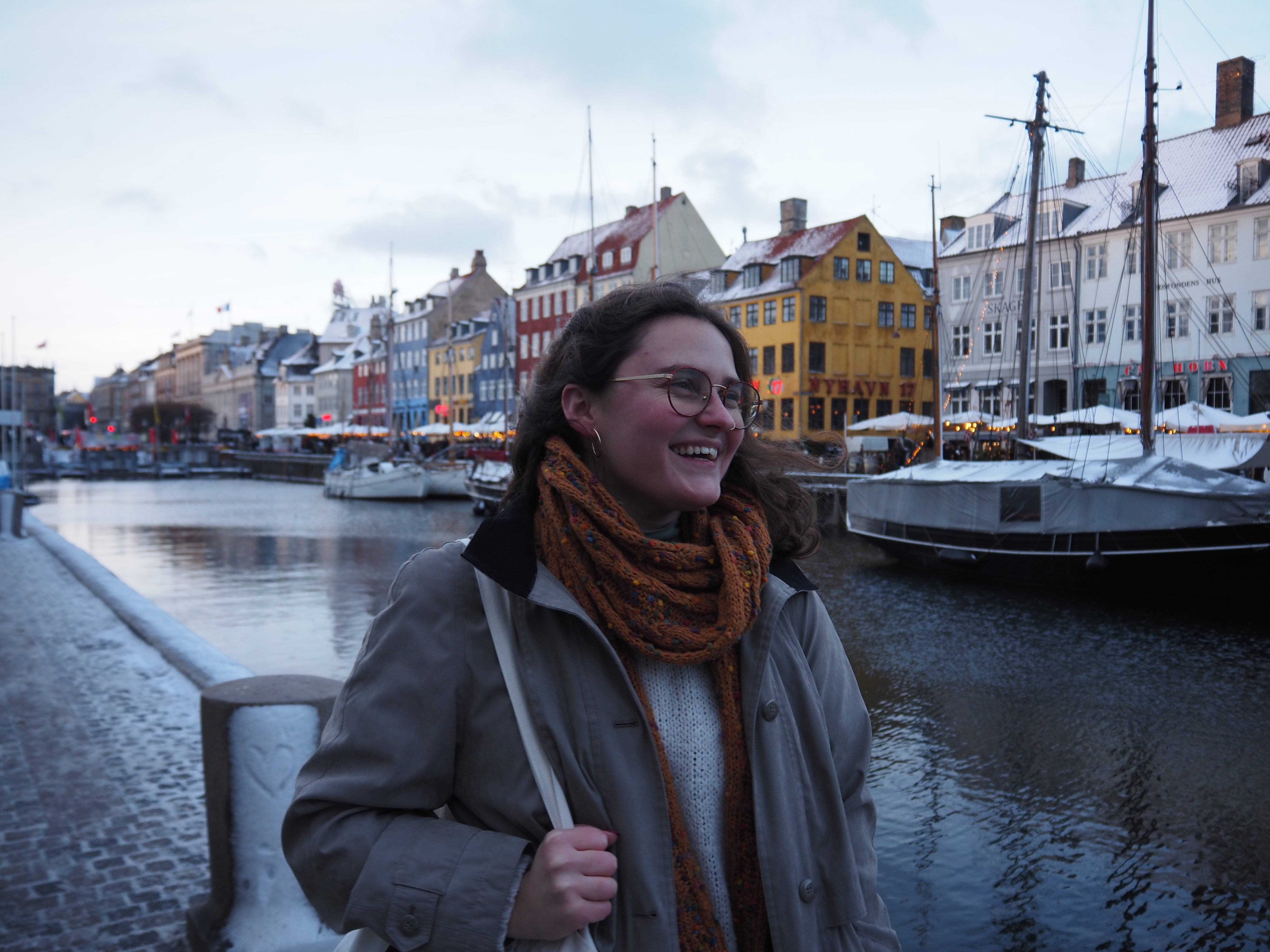 Diana smiling by a canal in Copenhagen with colorful buildings in the background