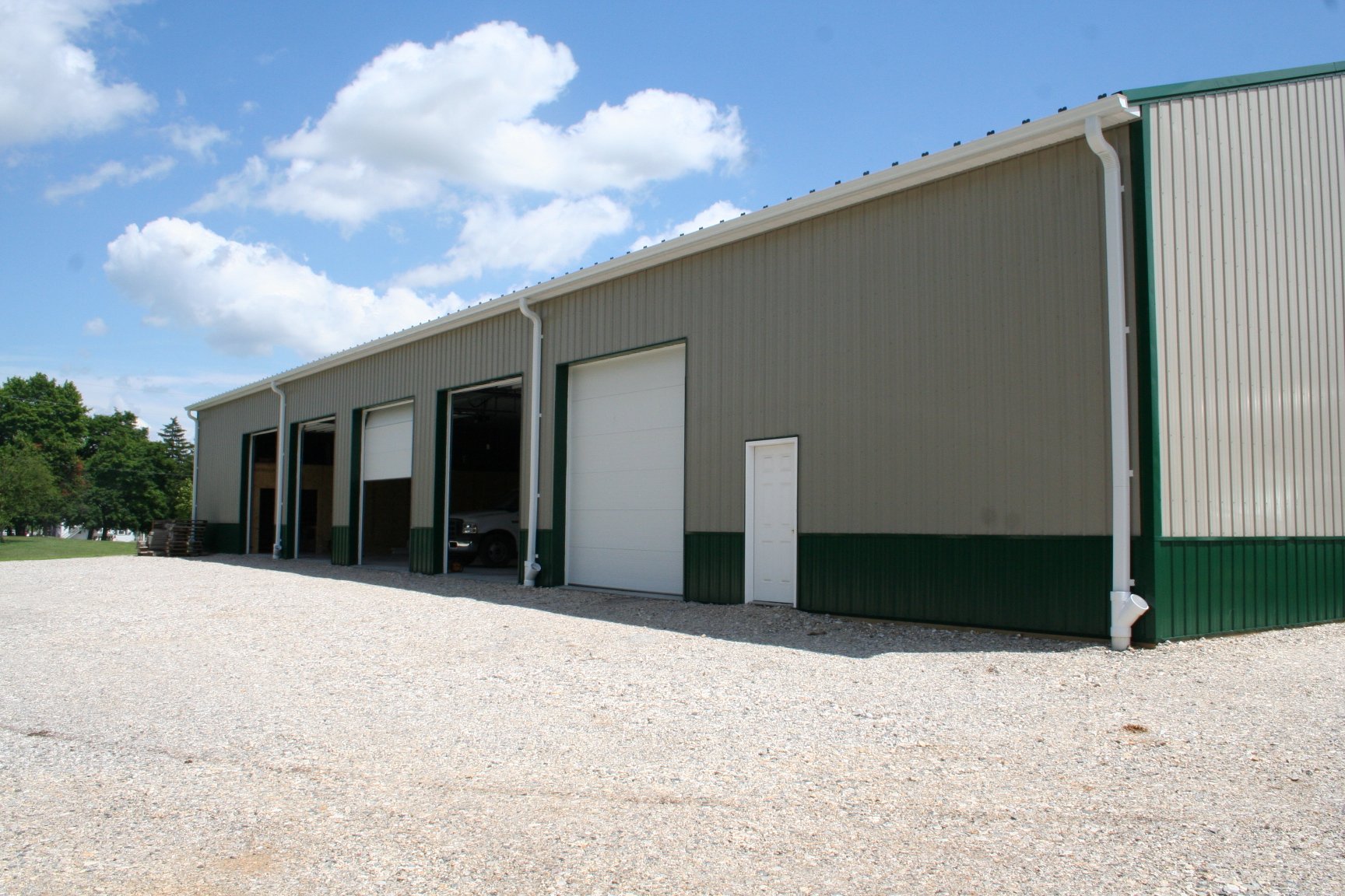 A large gray and green metal building with multiple garage doors and a car parked inside