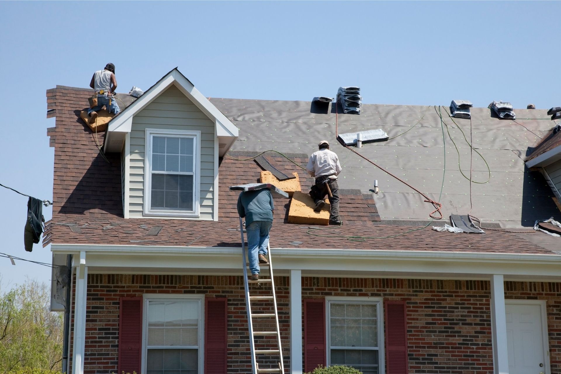 Three roofers working on a house roof under a blue sky
