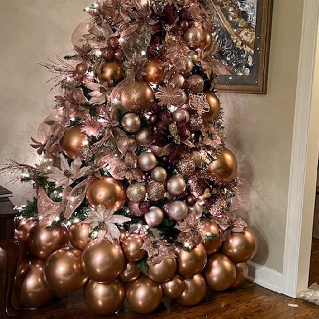 A luxurious Christmas tree adorned with gold and rose gold ornaments and balloons