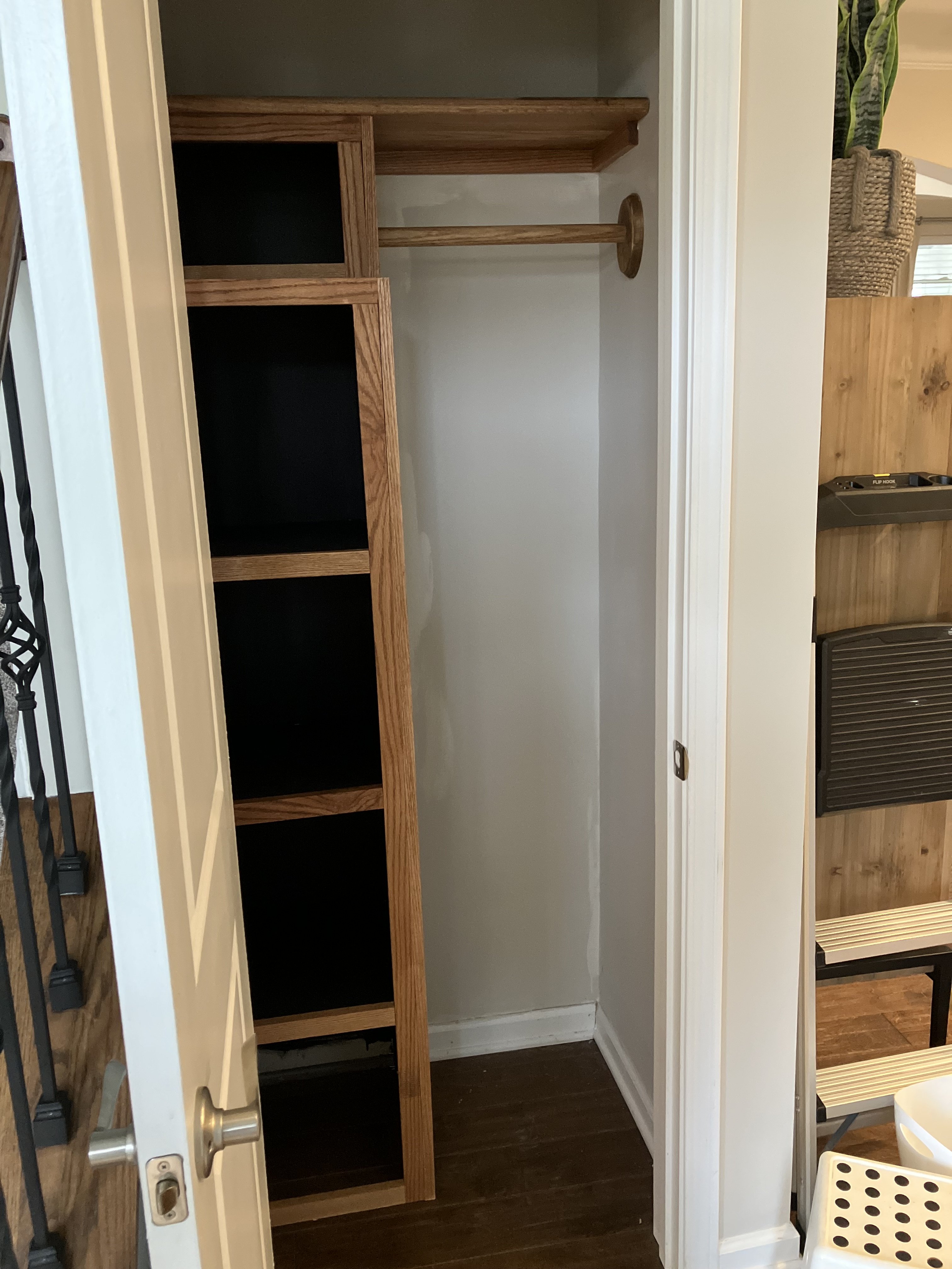 A small wooden closet with shelves and a hanging rod, viewed from the open door.