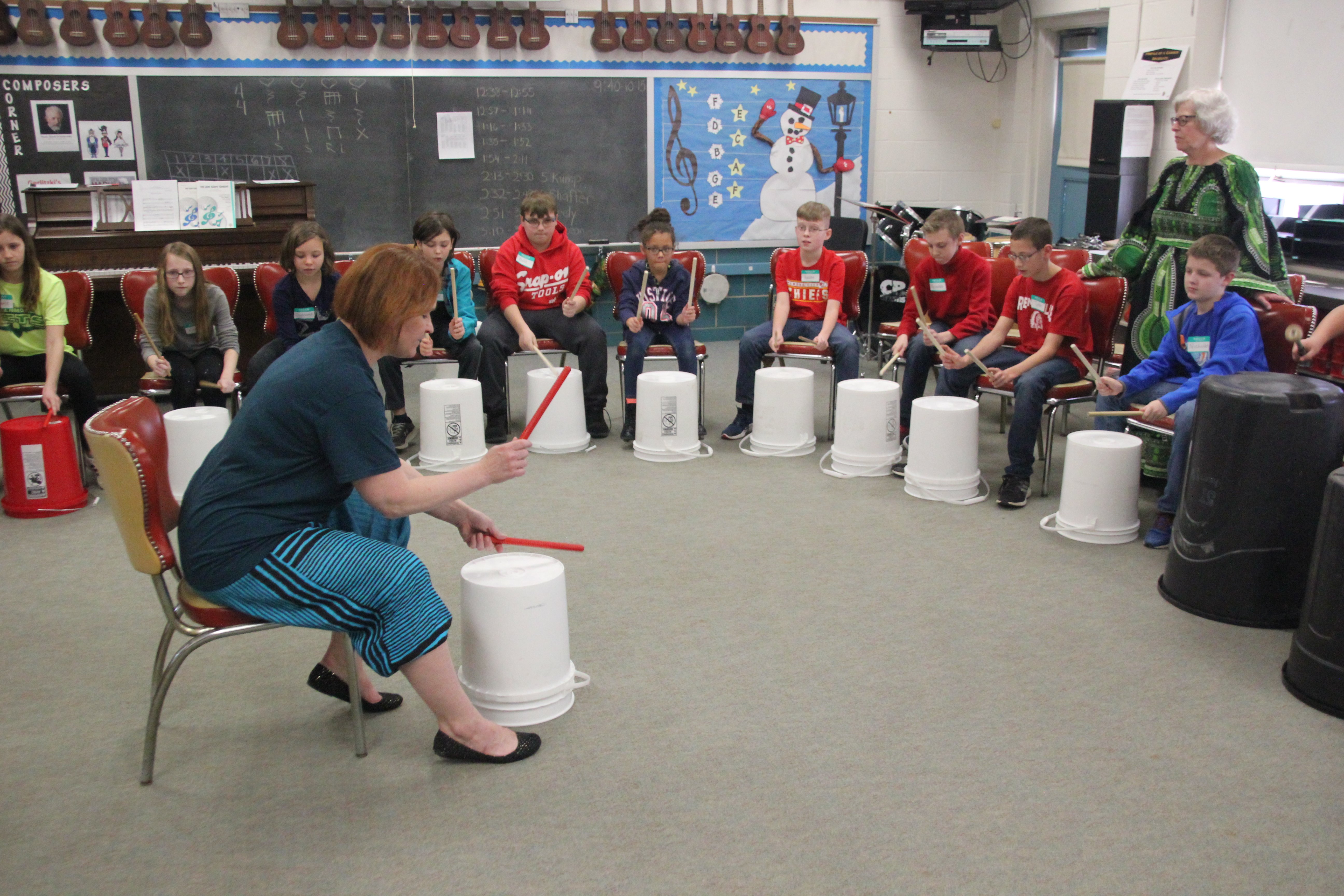 A group of children and adults playing drums in a classroom setting