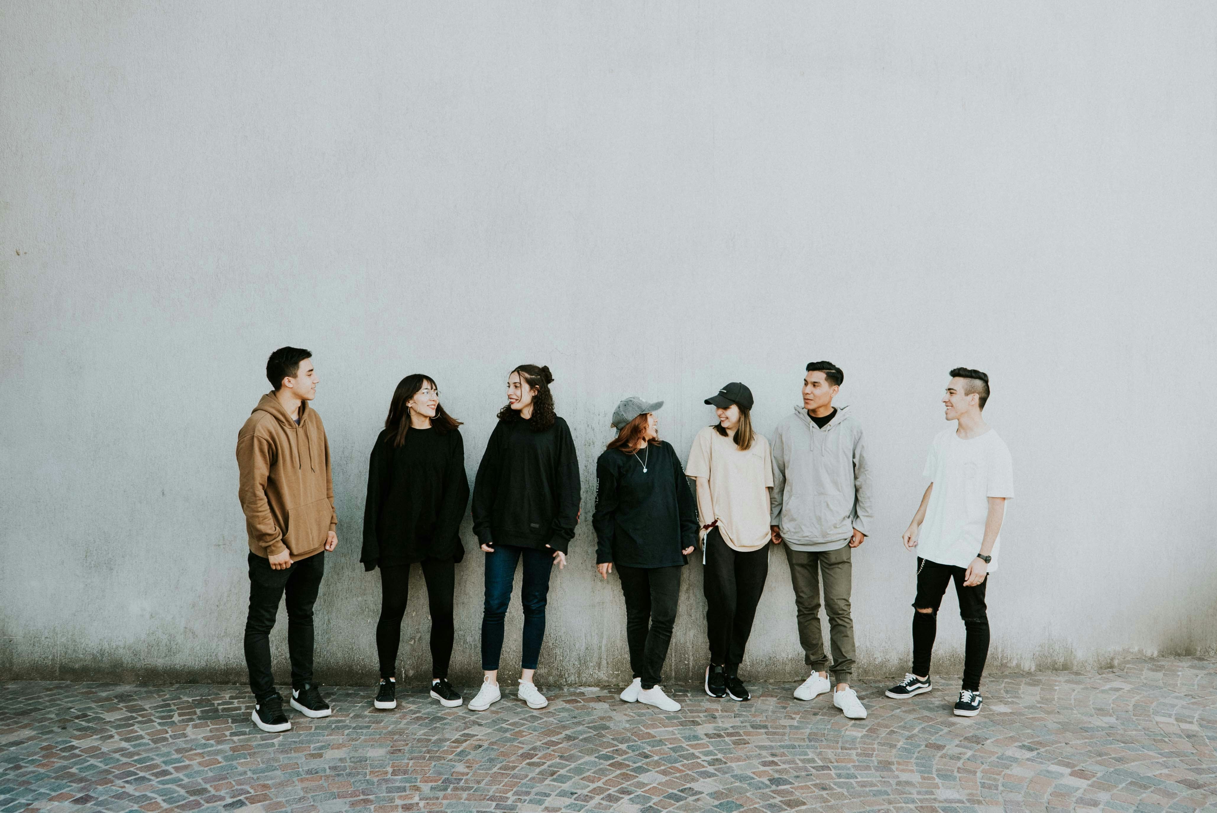 A group of six young adults standing in front of a white wall, smiling and looking at the camera