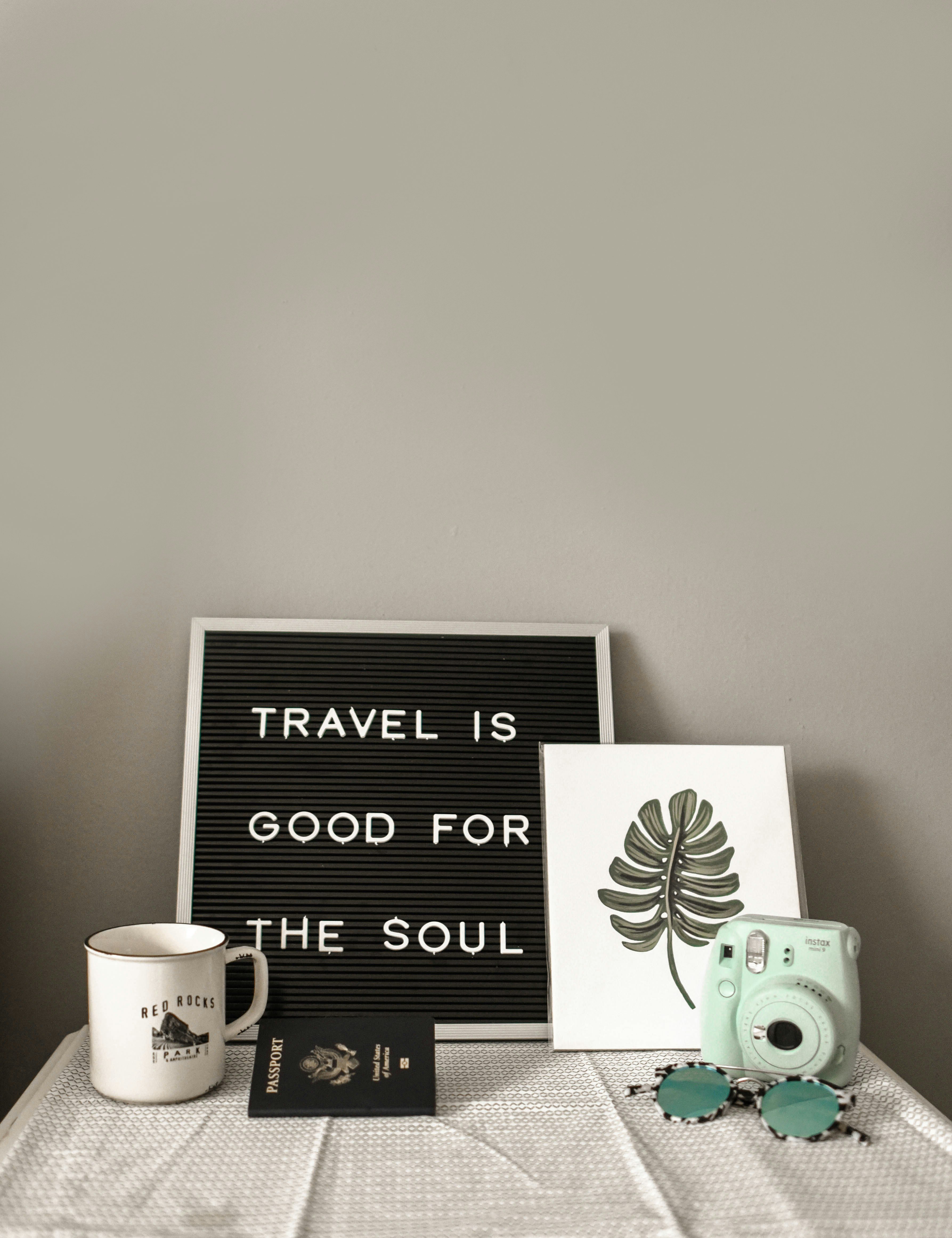 A desk with a mug, passport, and camera, with a sign saying 'Travel is good for the soul'.