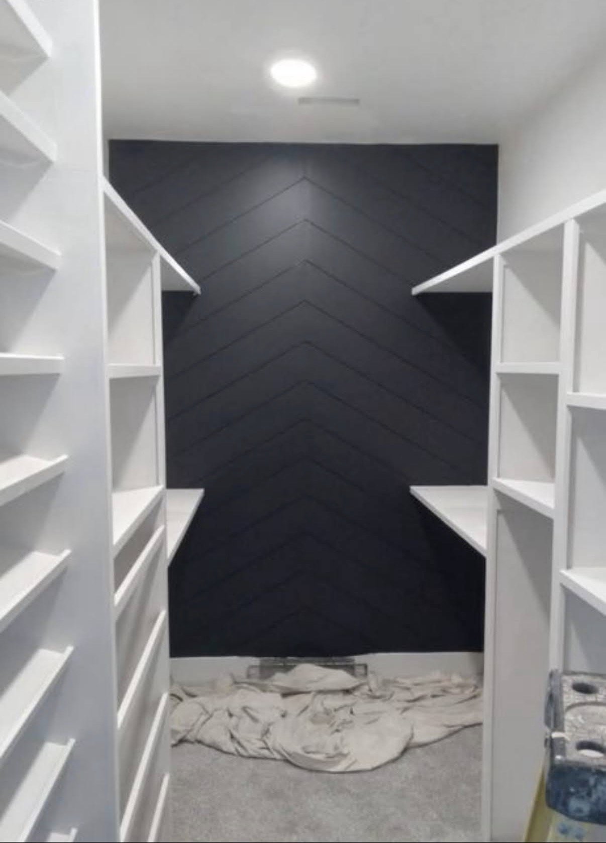 A modern walk-in closet with white shelves and a black chevron accent wall