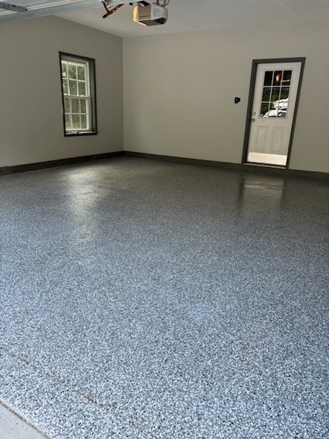 An empty garage with a newly installed gray epoxy floor and white walls