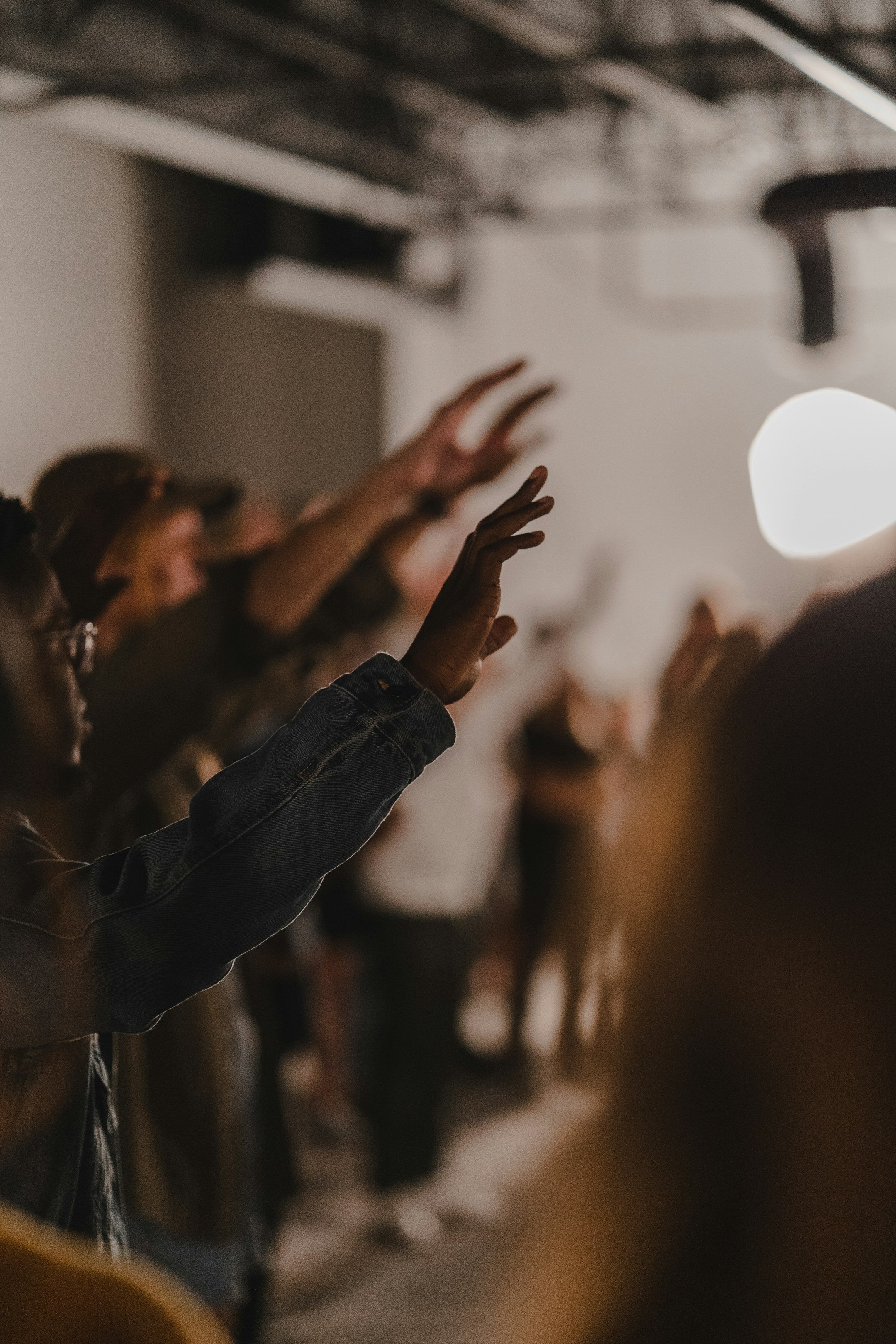 A group of people raising their hands in a room with a bright light in the background