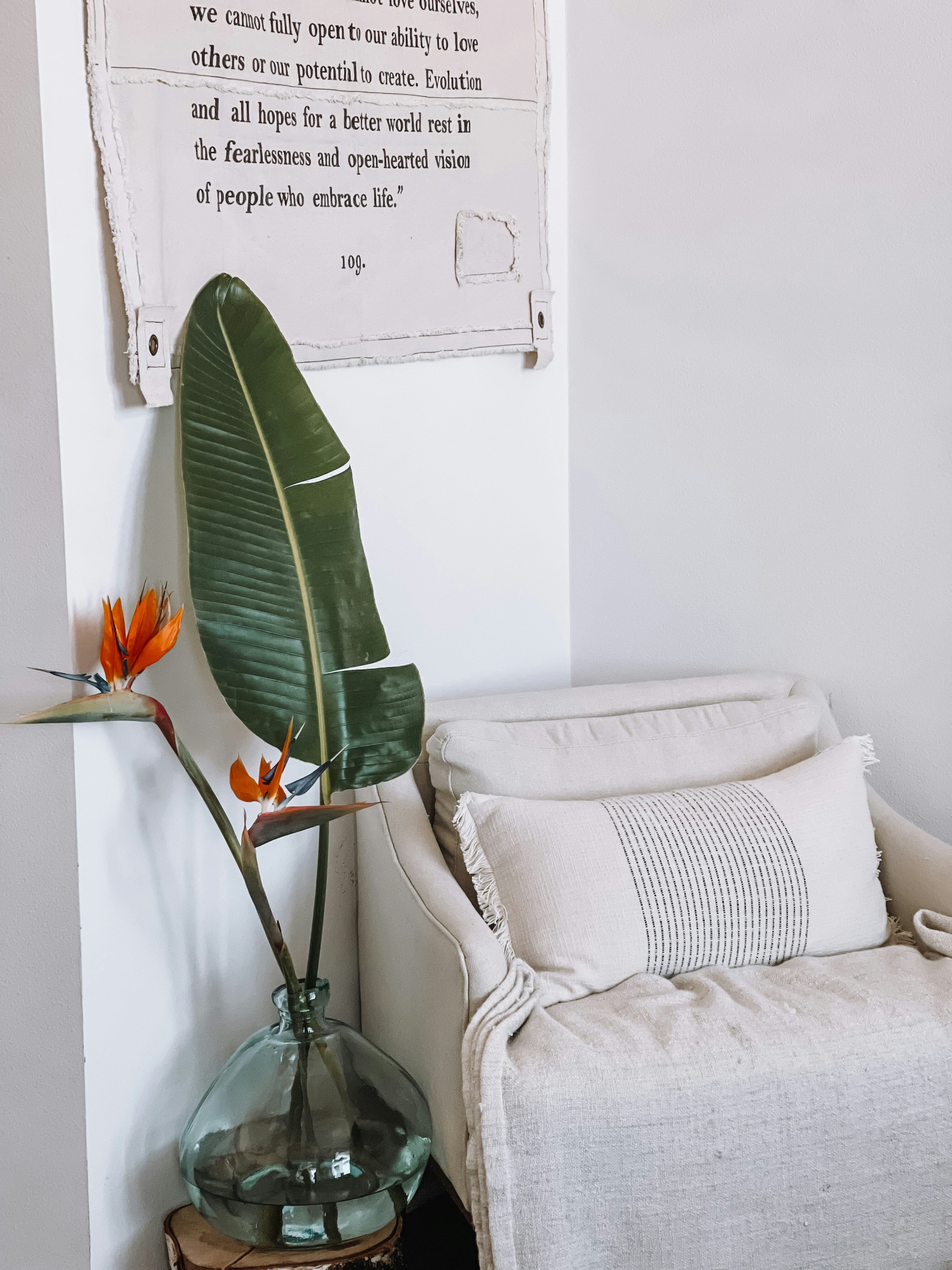 A white couch with a pillow and a plant in a glass vase on a wooden table