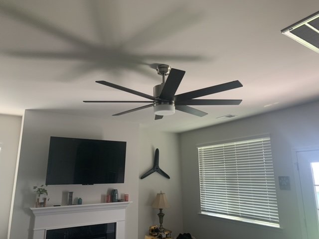 A modern living room with a ceiling fan, fireplace, and flat-screen TV