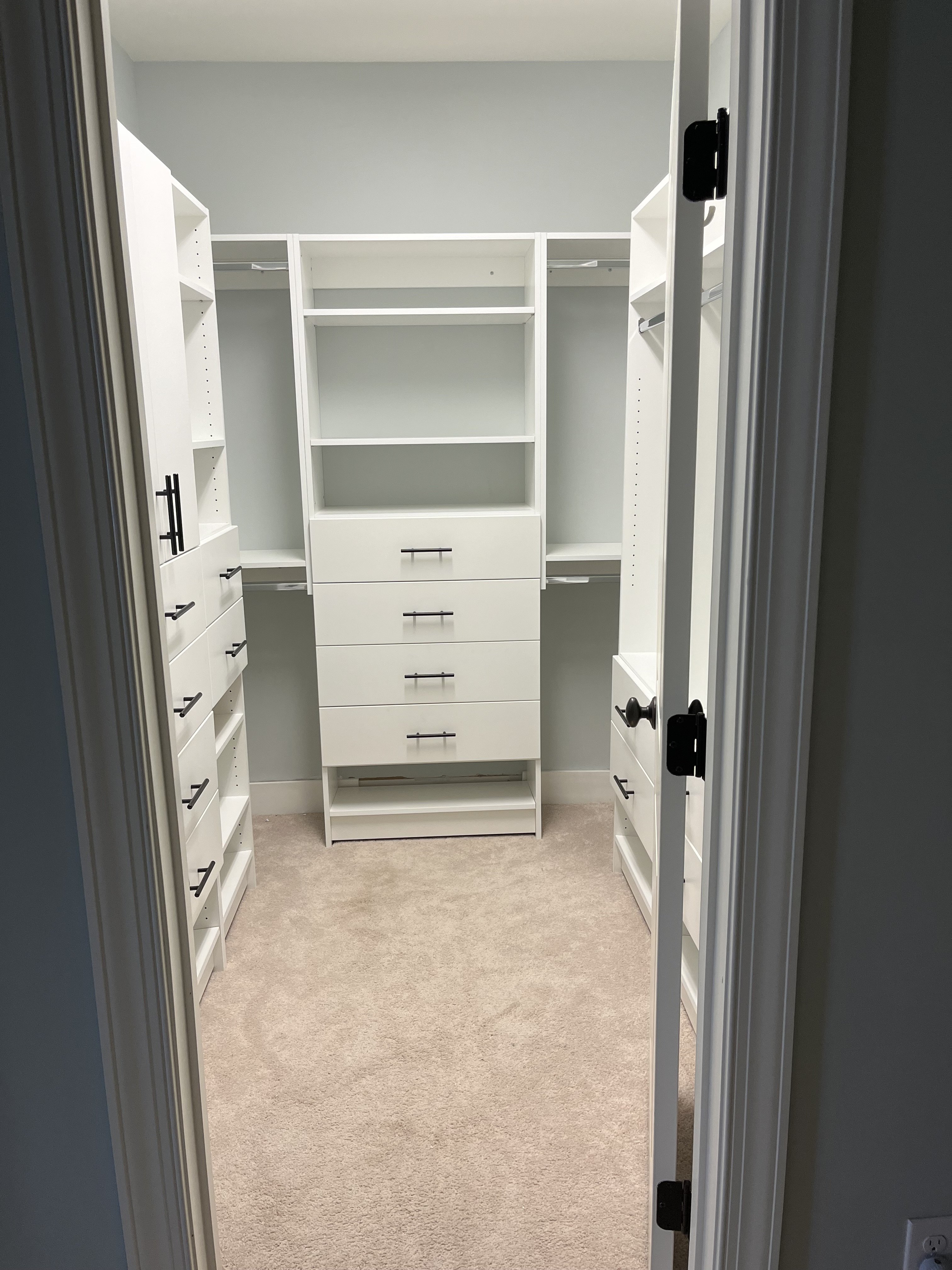 An empty walk-in closet with white shelves, drawers, and a beige carpet
