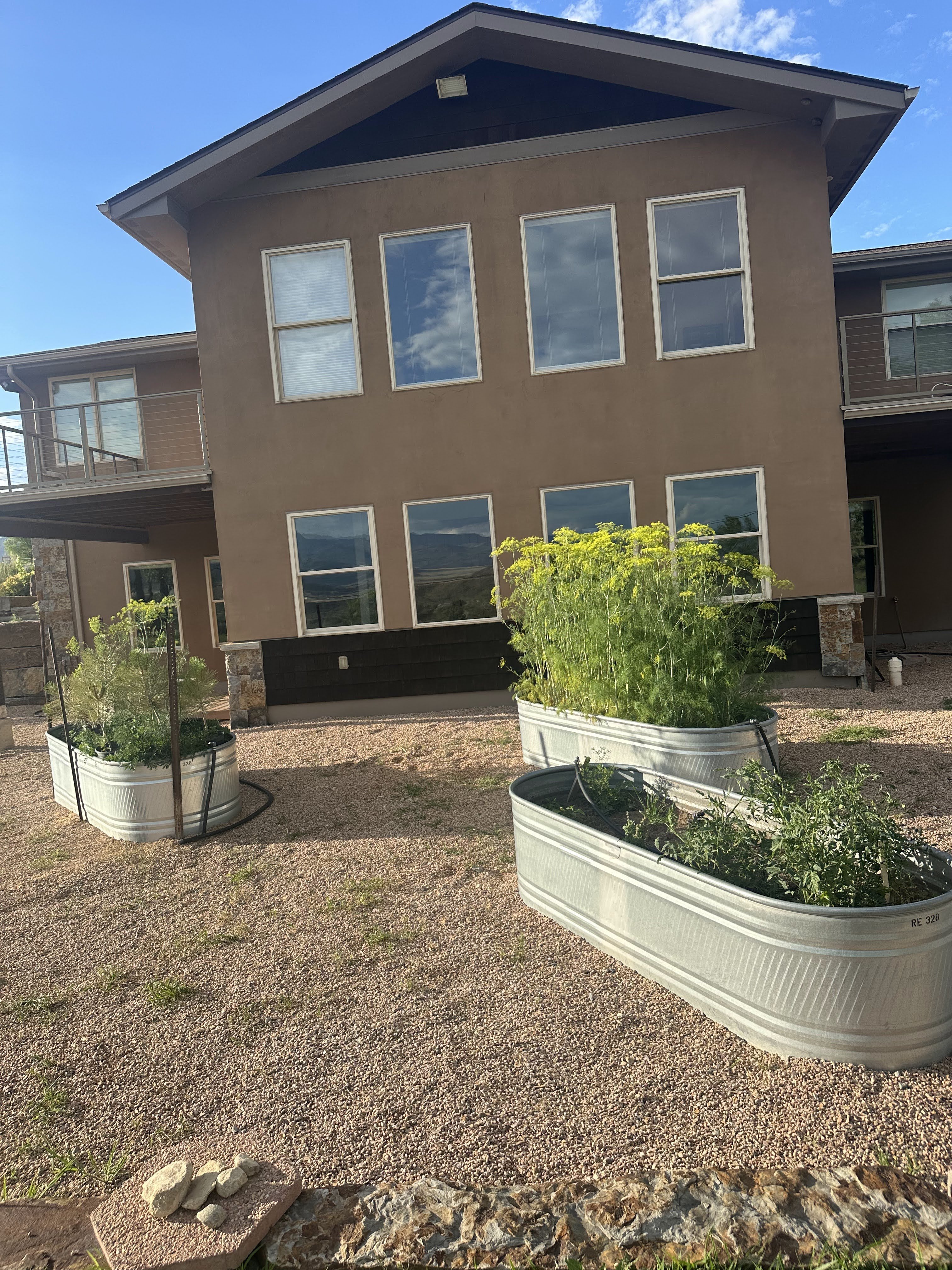 A modern house with a balcony and three large metal planters with plants in front of it