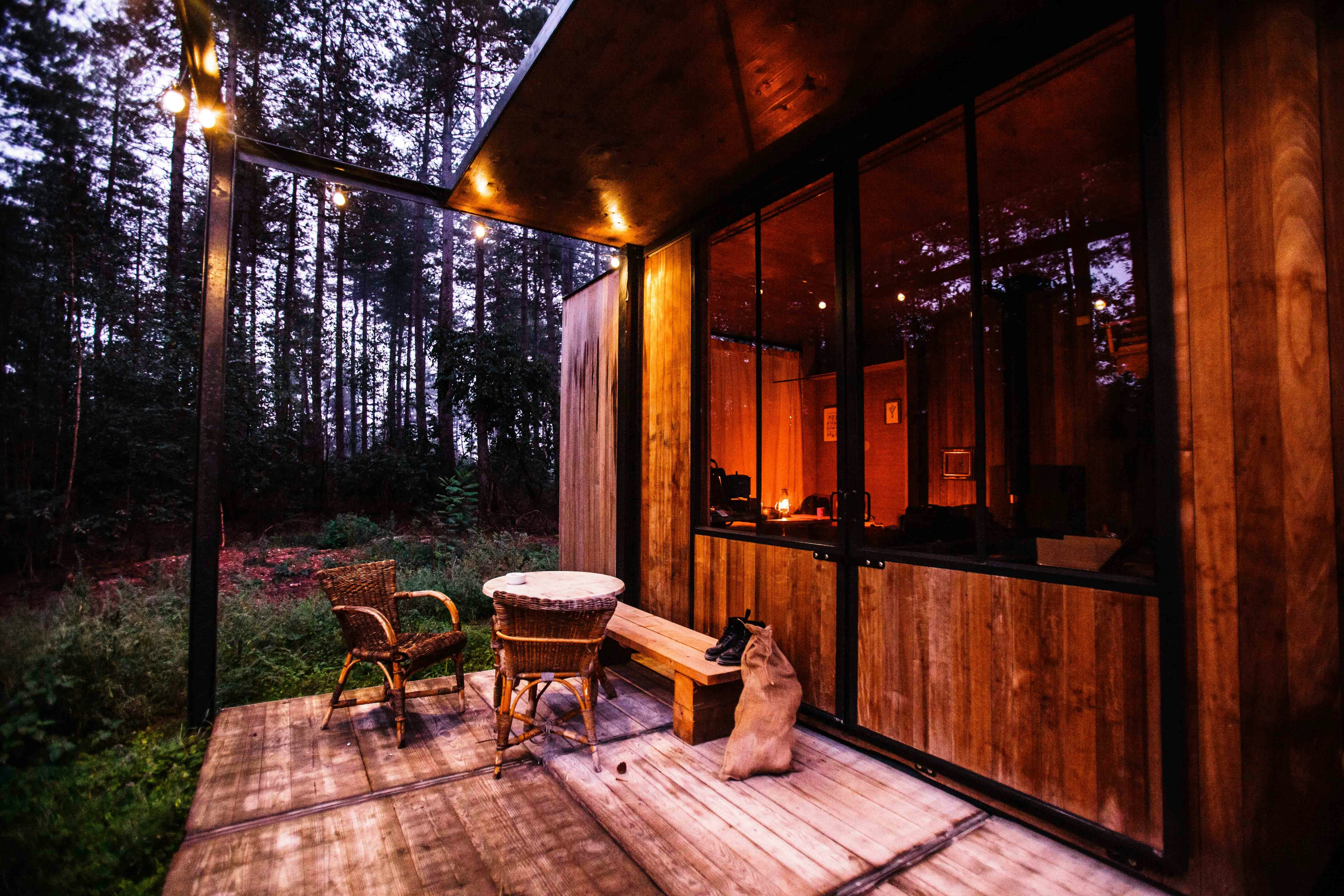 A cozy wooden cabin with a porch, surrounded by a forest at dusk