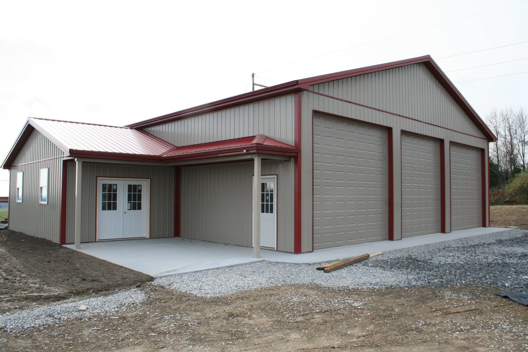 A gray metal building with red trim and three garage doors, under a cloudy sky