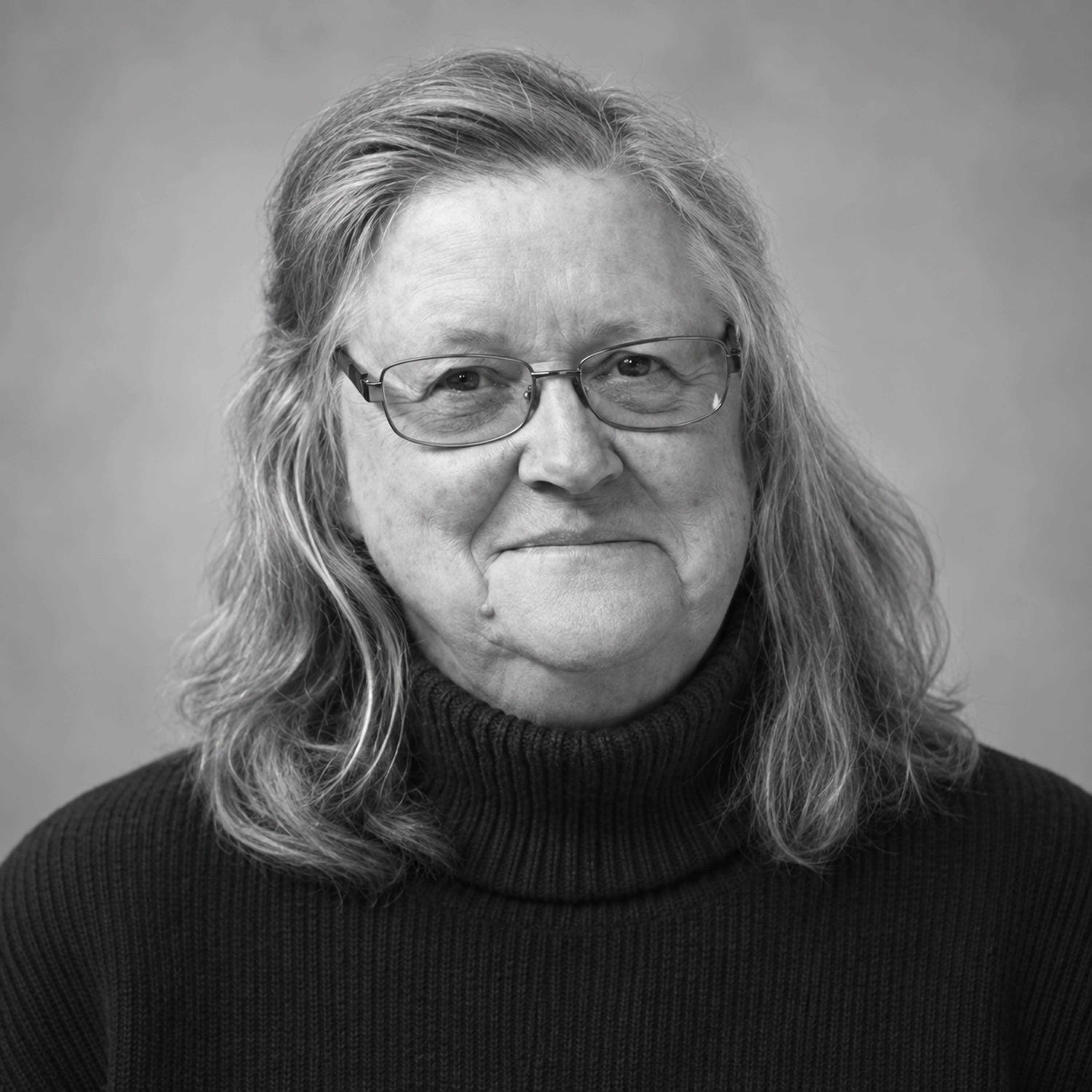 An older woman with long gray hair wearing glasses and a black turtleneck