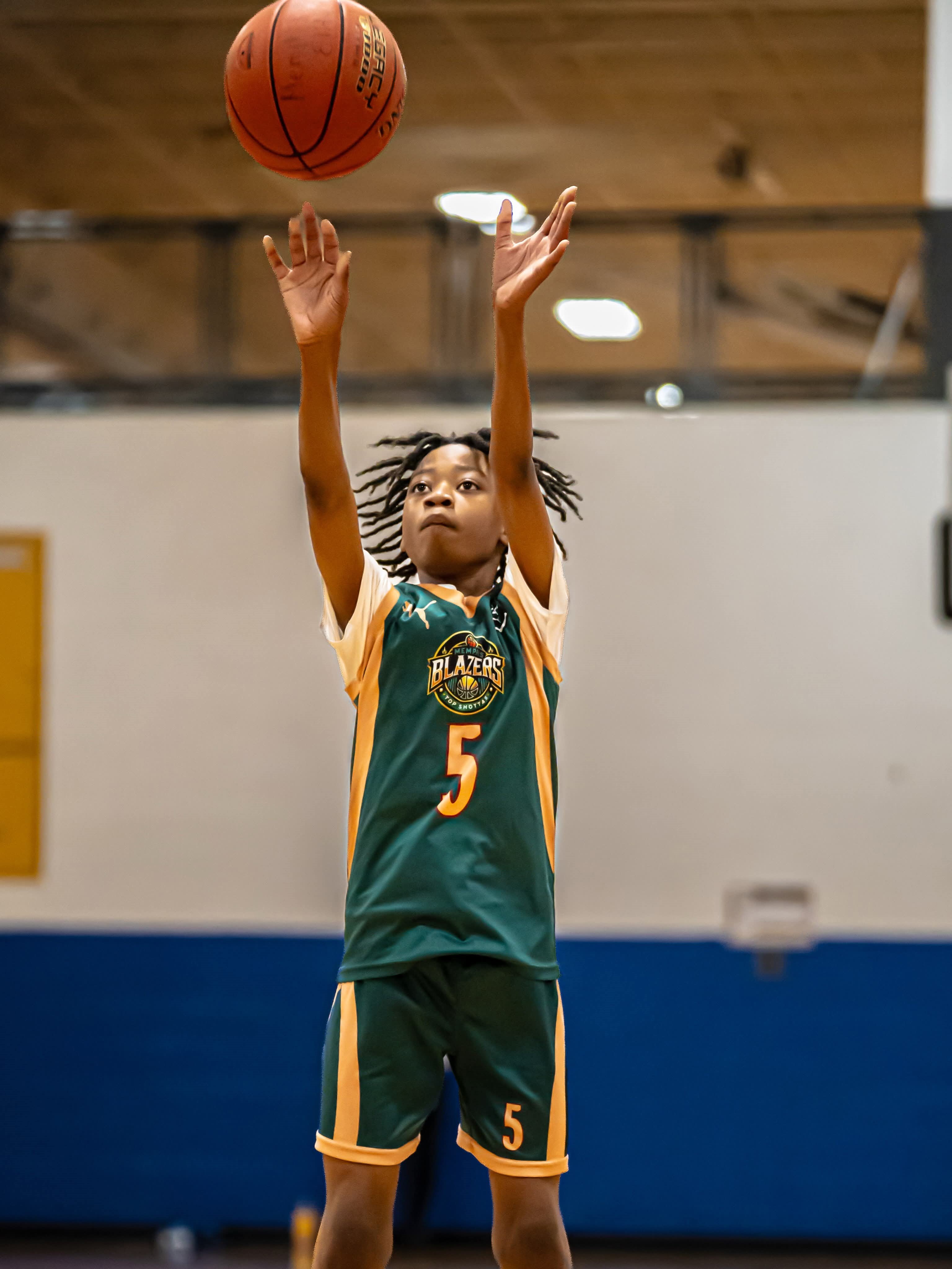 13U E.J. - A young basketball player in a green jersey with the number 5 jumps to shoot the ball