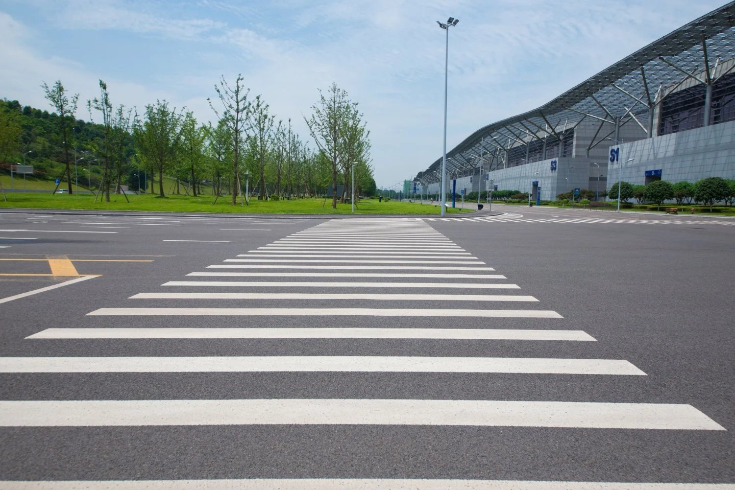 An empty parking lot with white crosswalk markings and a large building in the background