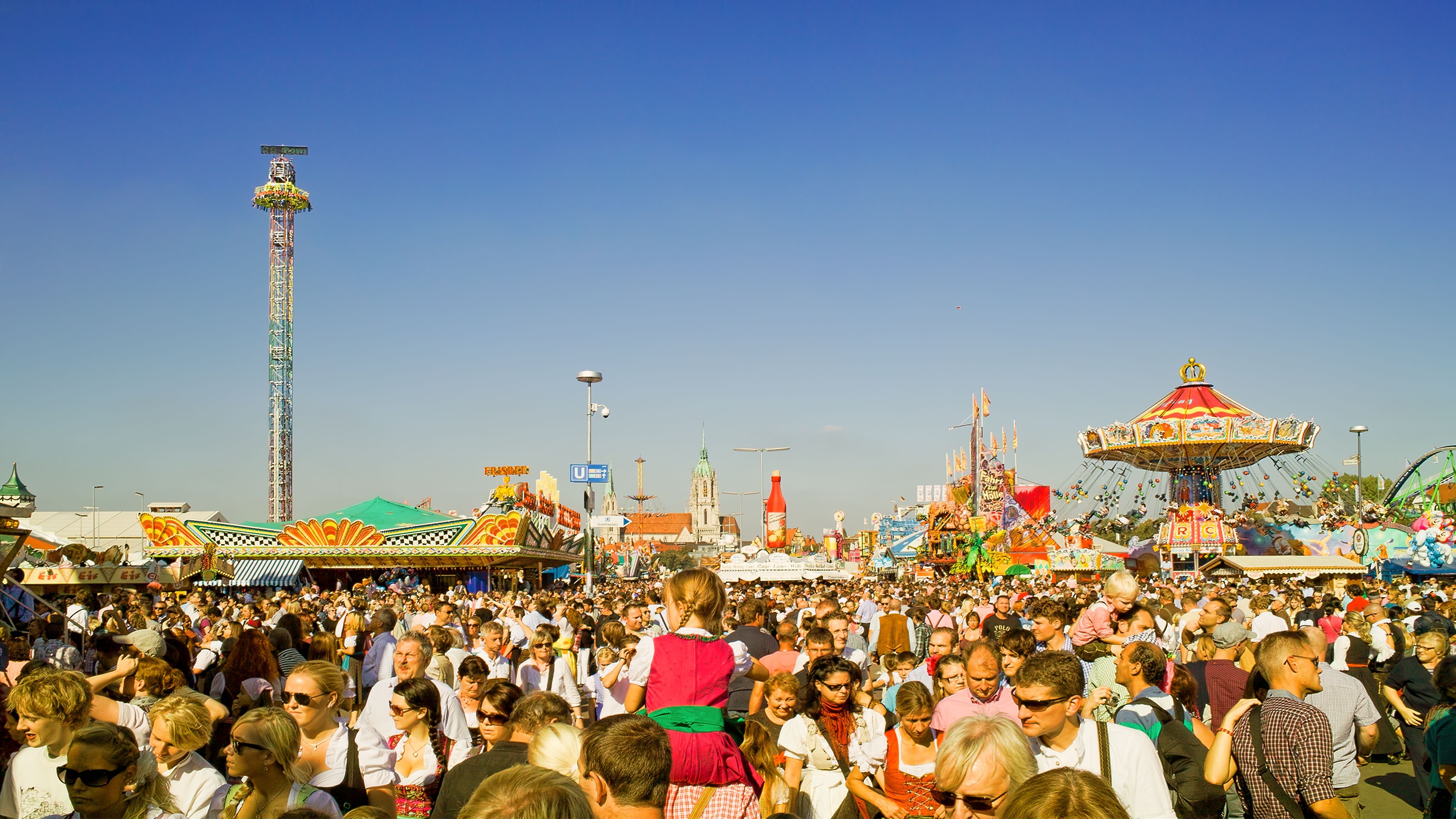 A large crowd of people at an outdoor amusement park with rides and attractions