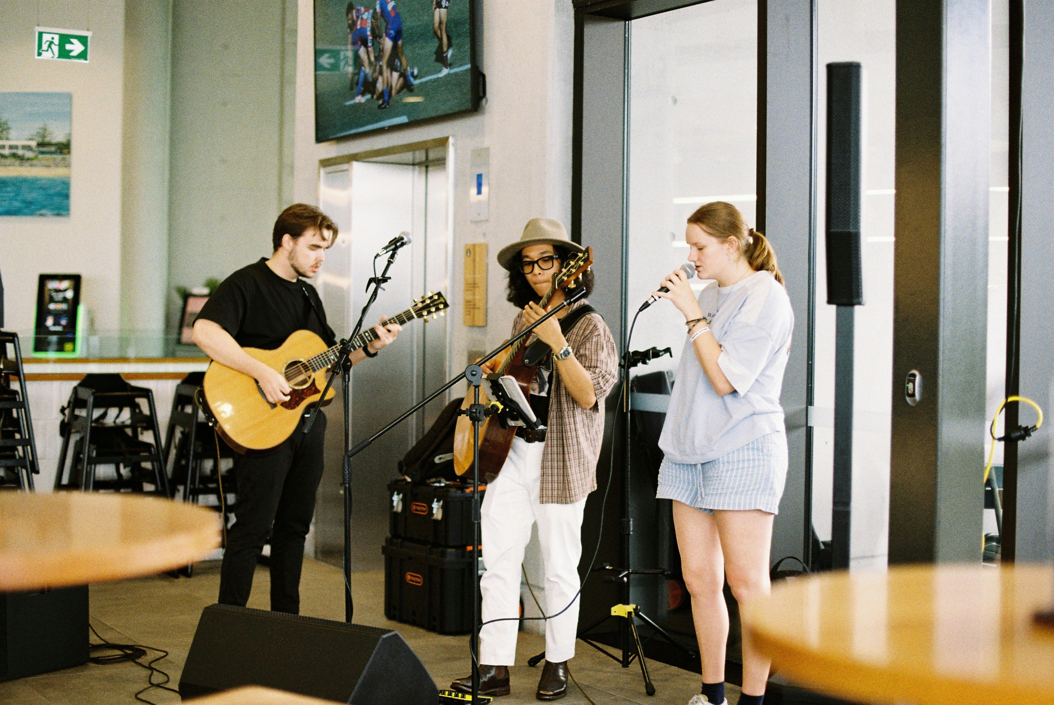 Three musicians perform with guitars and microphones in a modern, open space.