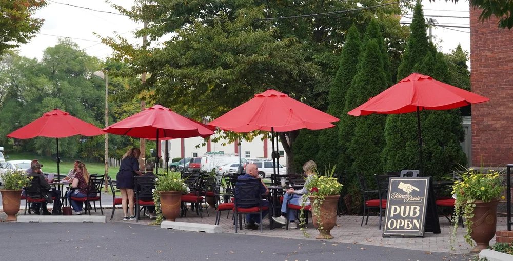 Outdoor seating area at a pub with red umbrellas and people sitting at tables