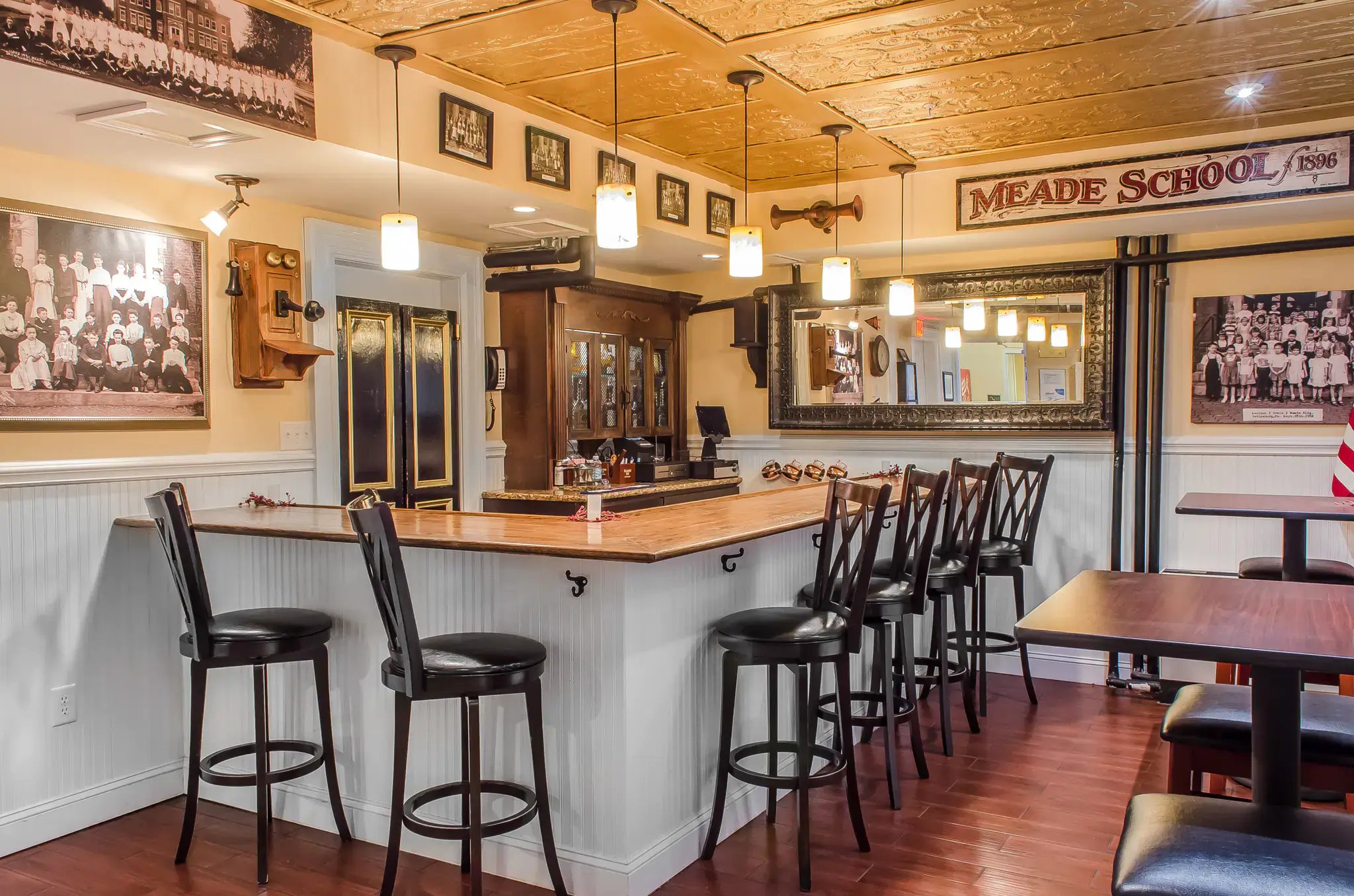 A bar area with wooden bar stools, a wooden bar counter, and a vintage-style telephone on the wall.