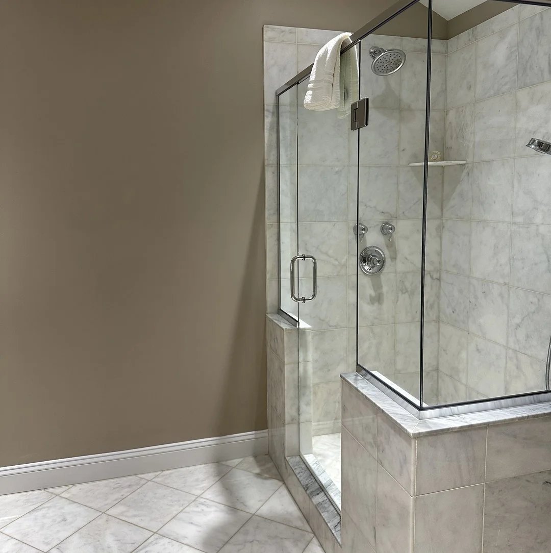A luxurious marble shower with a glass door and a towel hanging on the wall