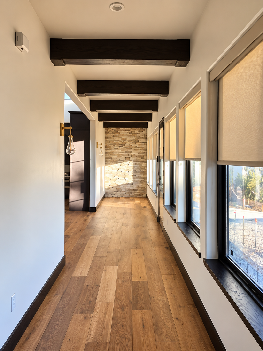 A modern hallway with wooden floors, brick wall, and large windows with blinds