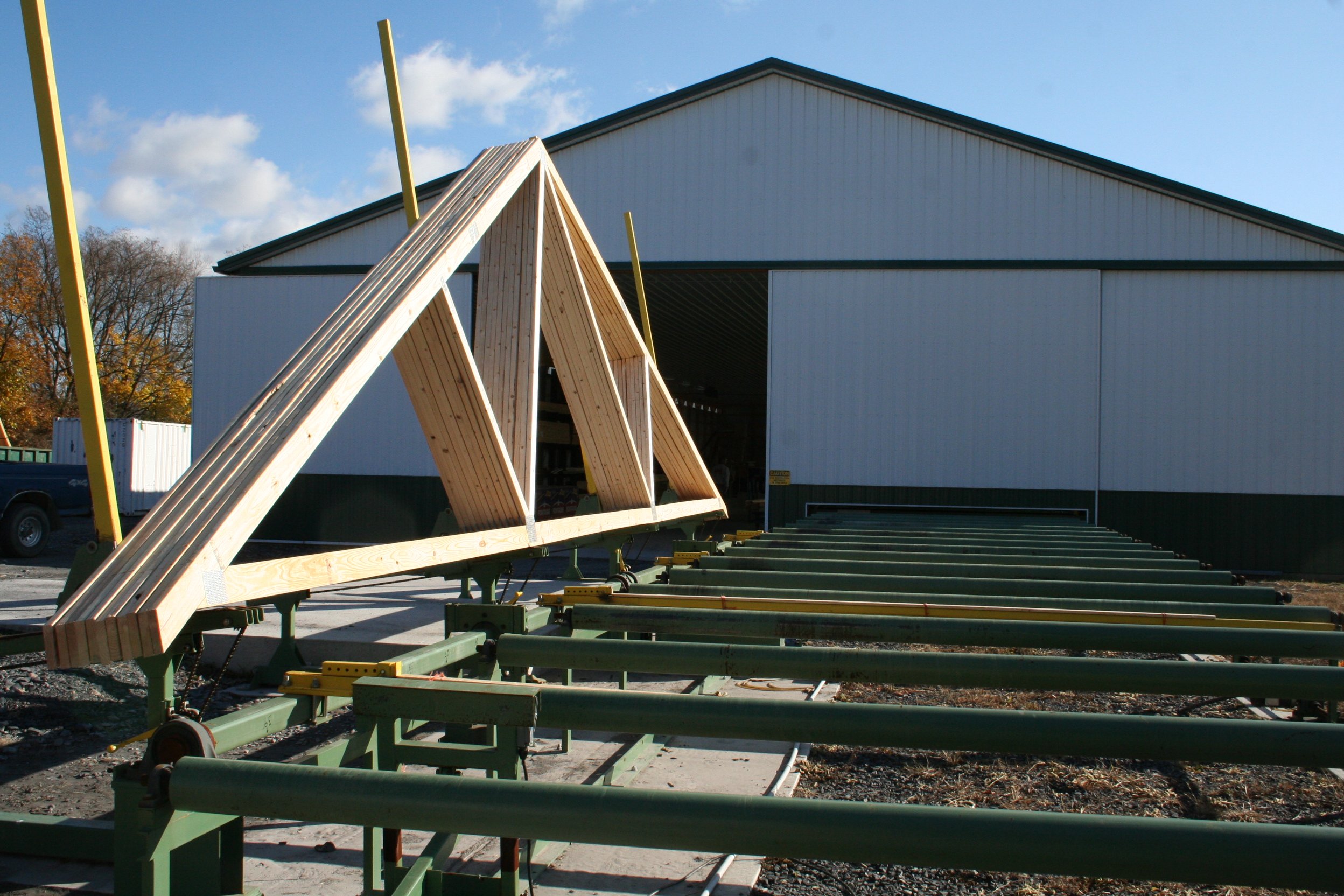 A wooden truss structure being assembled outside a large white building with a green trim