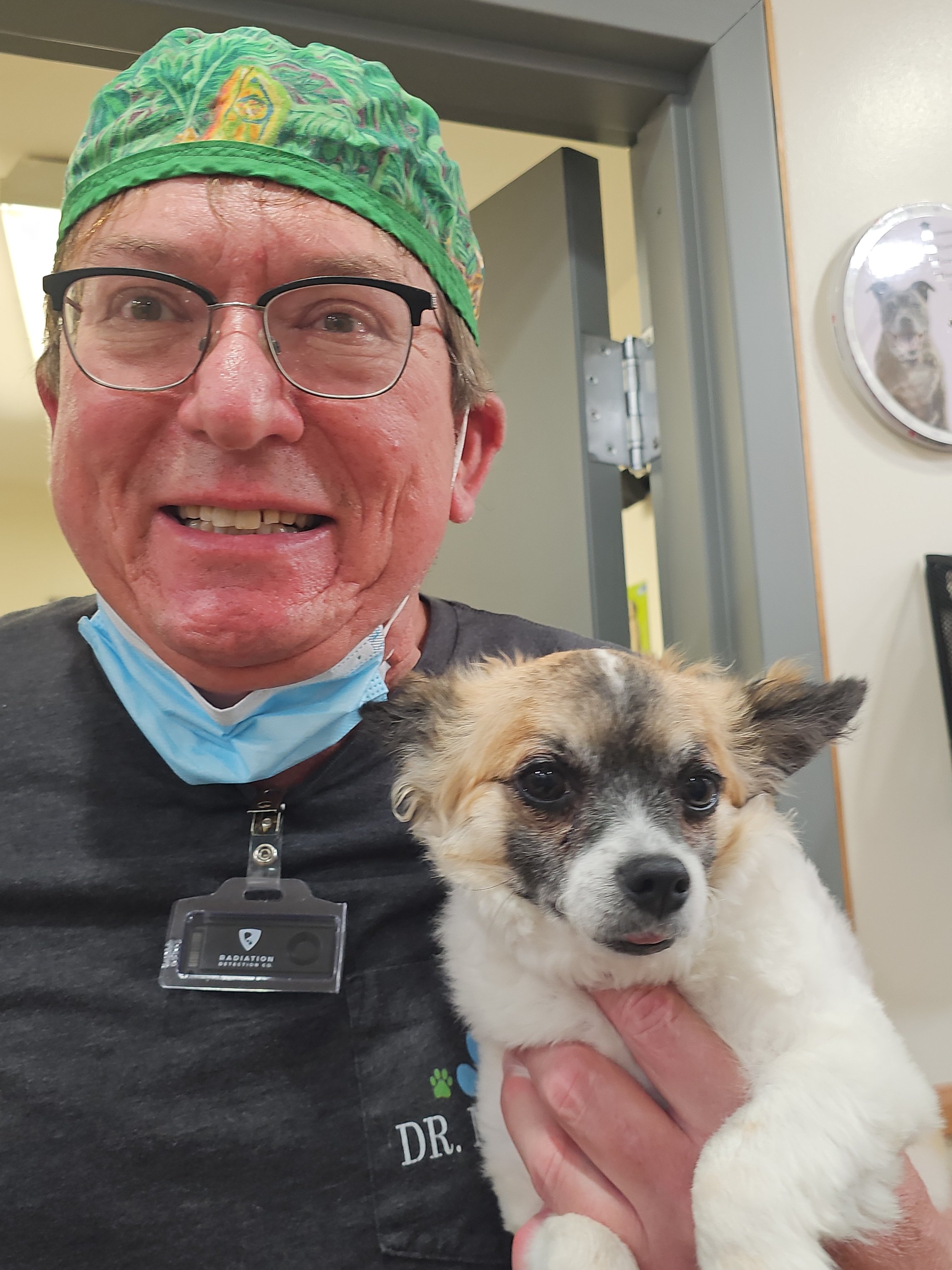 Dr. Dan, wearing a green hat and glasses, holds a small dog named Bandit.