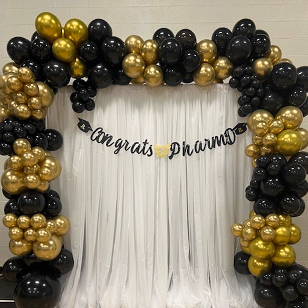 A black and gold balloon arch with a white backdrop and a banner saying 'Congratulations'