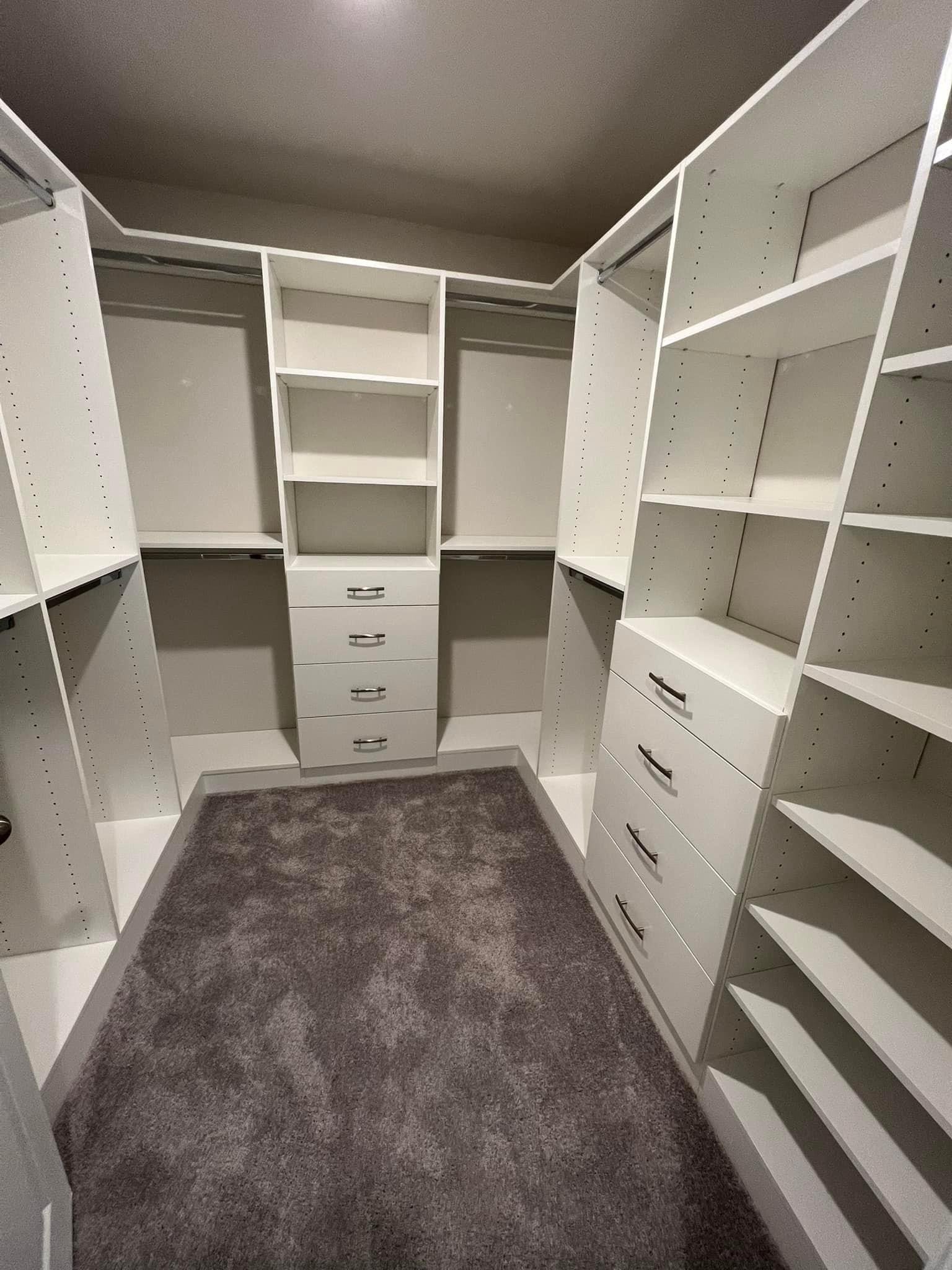 A spacious walk-in closet with white shelves, drawers, and a gray carpet floor