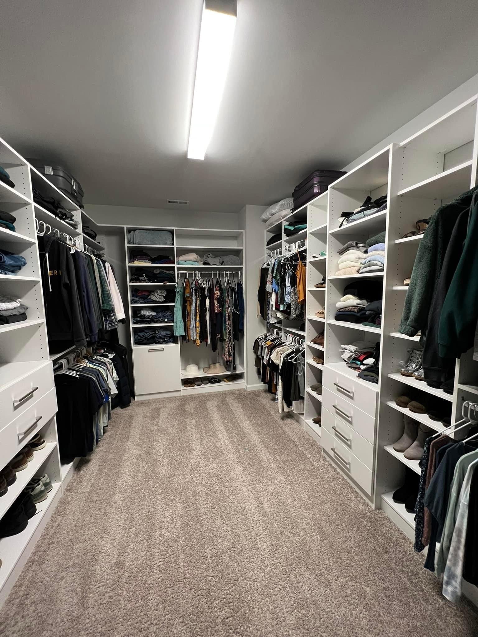 A spacious walk-in closet with white shelves and carpeted floor, filled with neatly organized clothes and accessories.