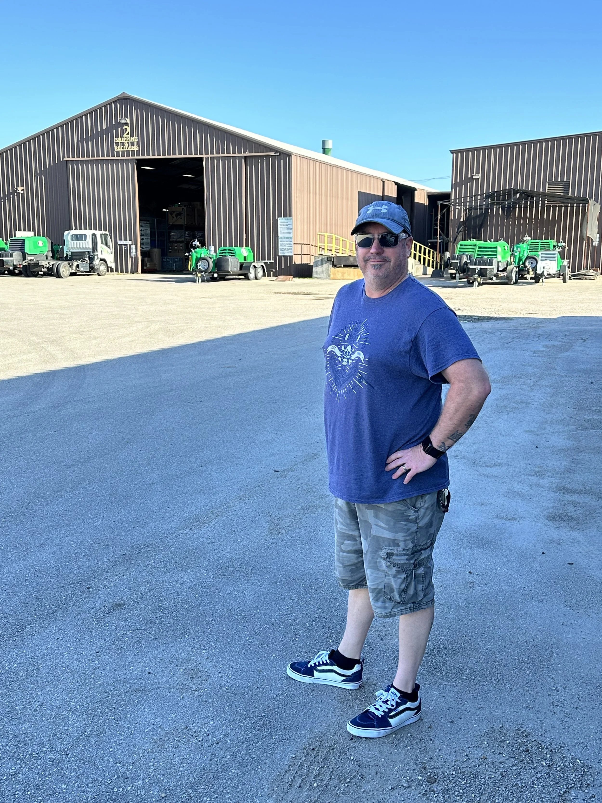 Dan Healy stands in front of a large building with machinery vehicles parked outside