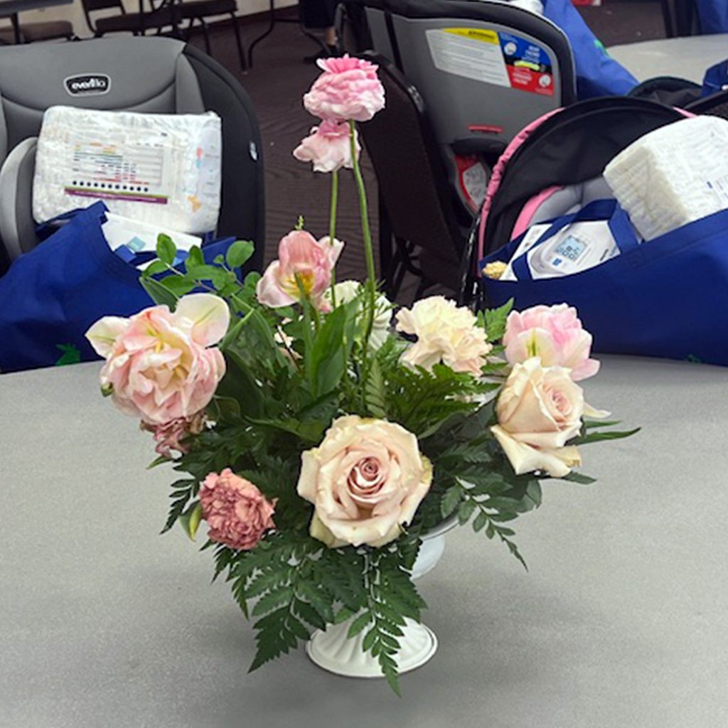 A white vase with pink and white roses and greenery on a table