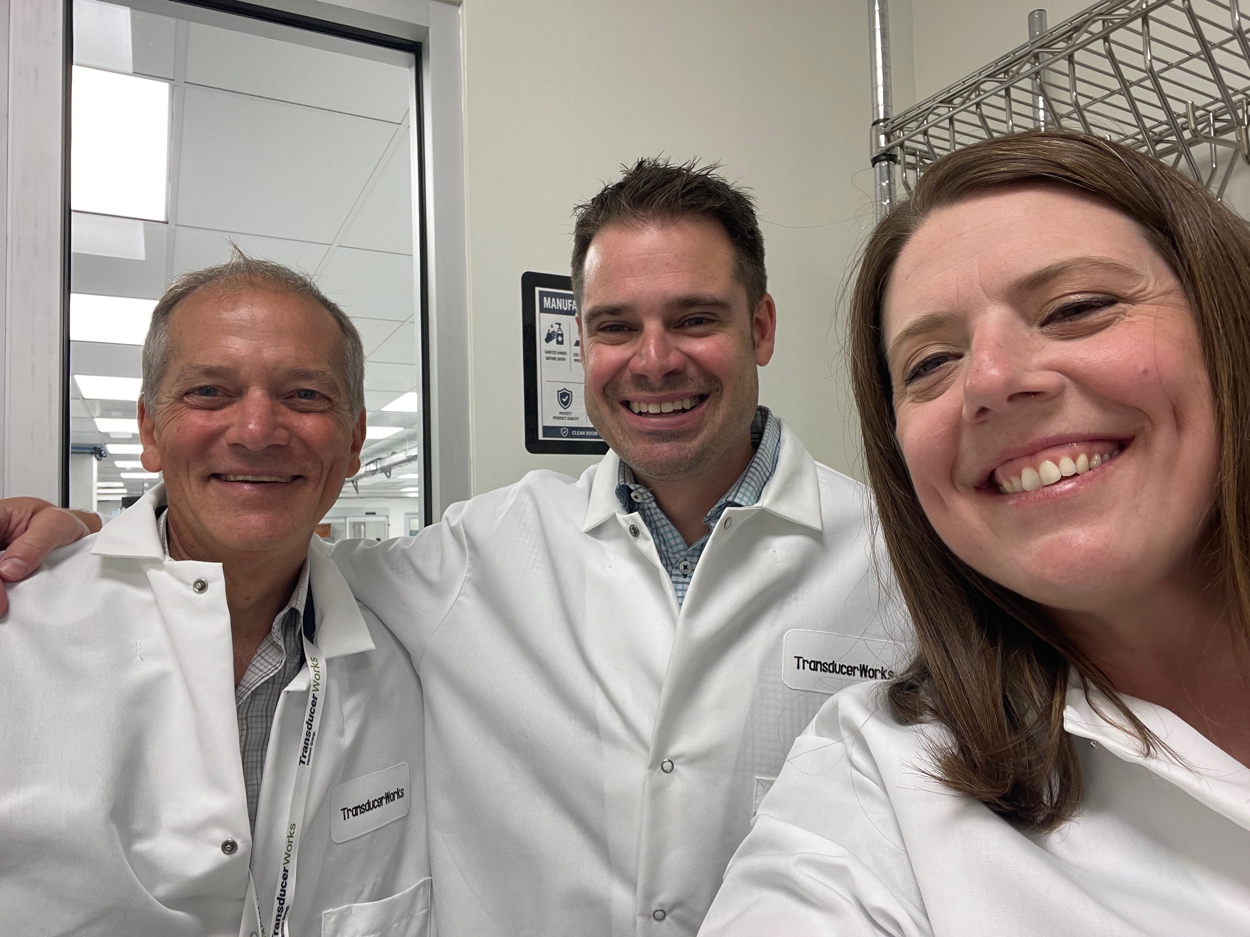 Three individuals in lab coats smiling for a photo in a lab setting