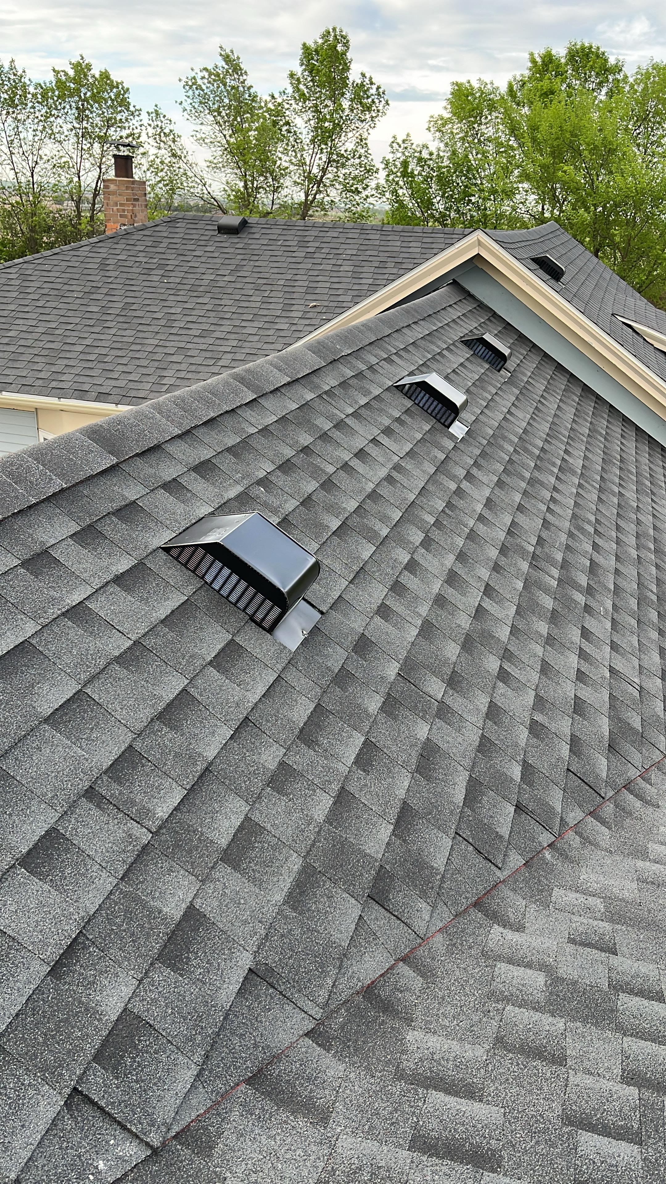 A gray shingled roof with vents and a chimney on a cloudy day