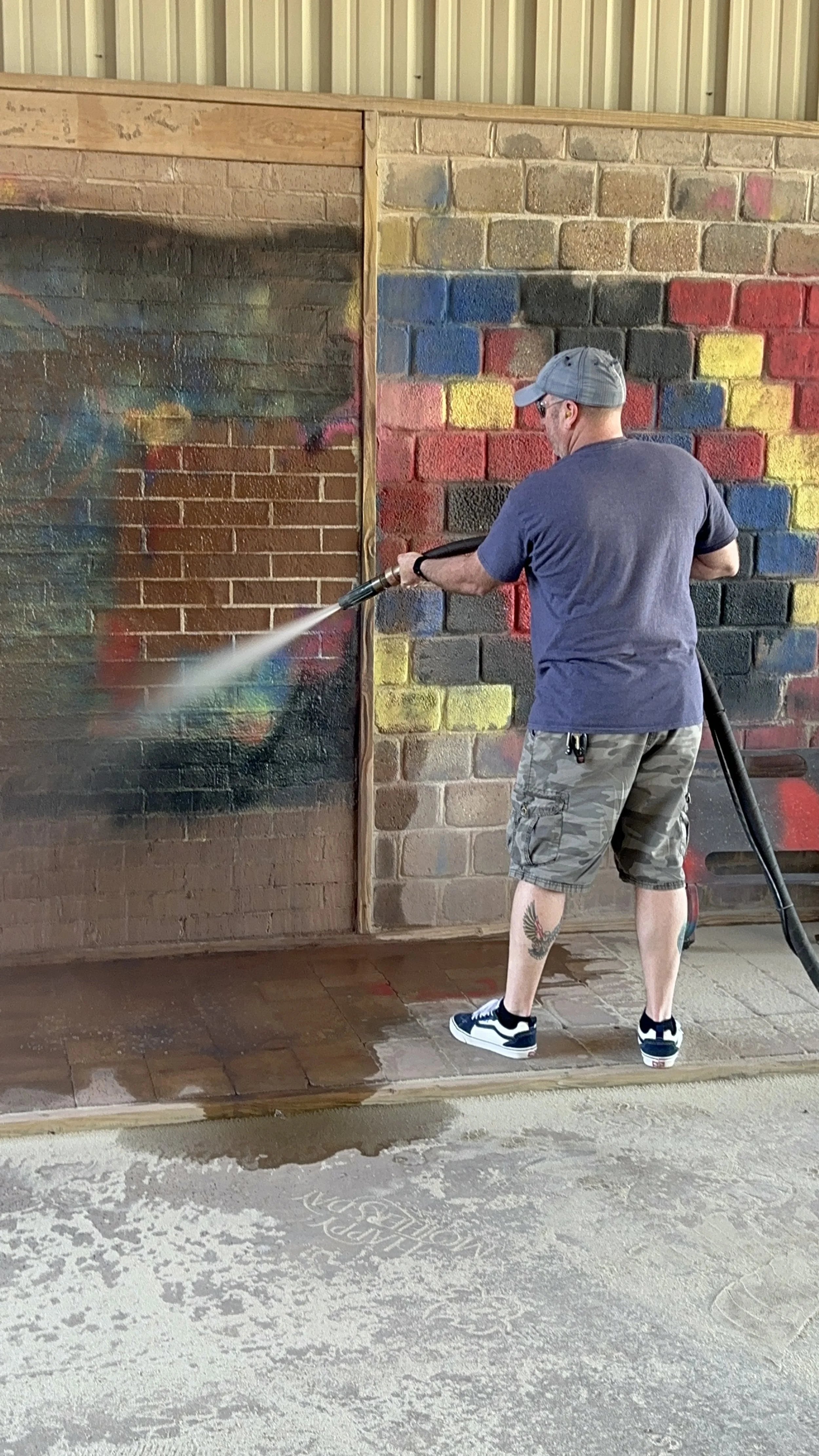 A man cleaning graffiti off a brick wall with a pressure washer