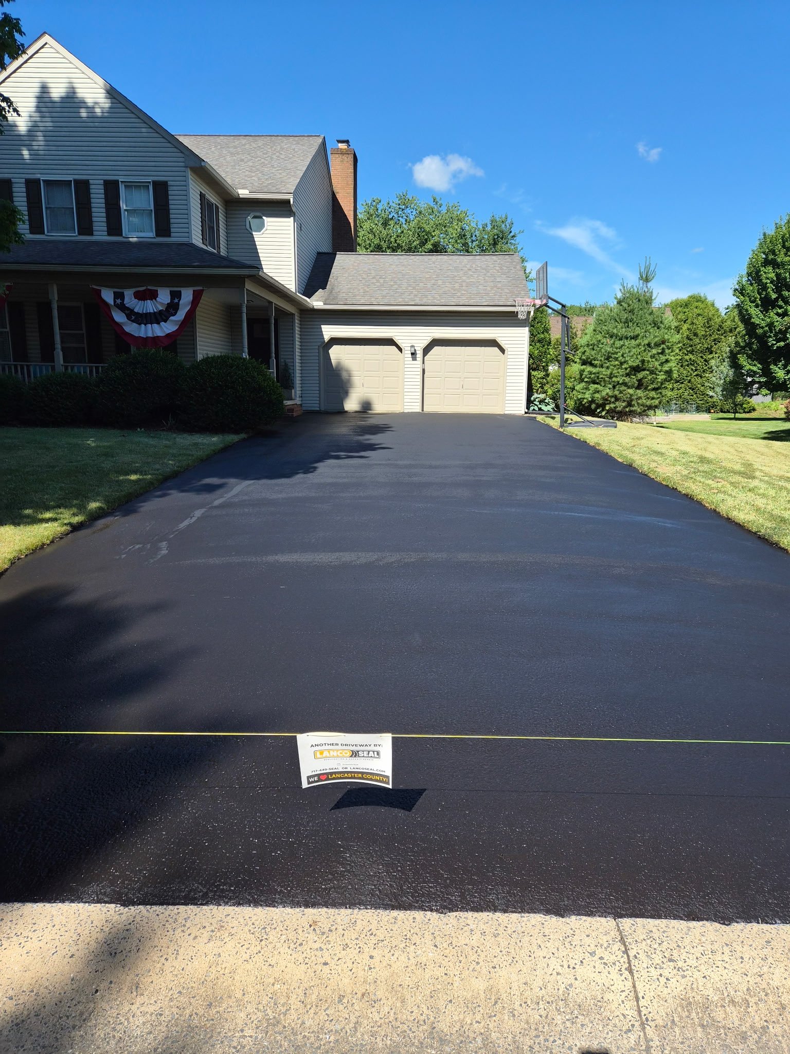 A newly paved driveway in front of a house with a basketball hoop and American flag