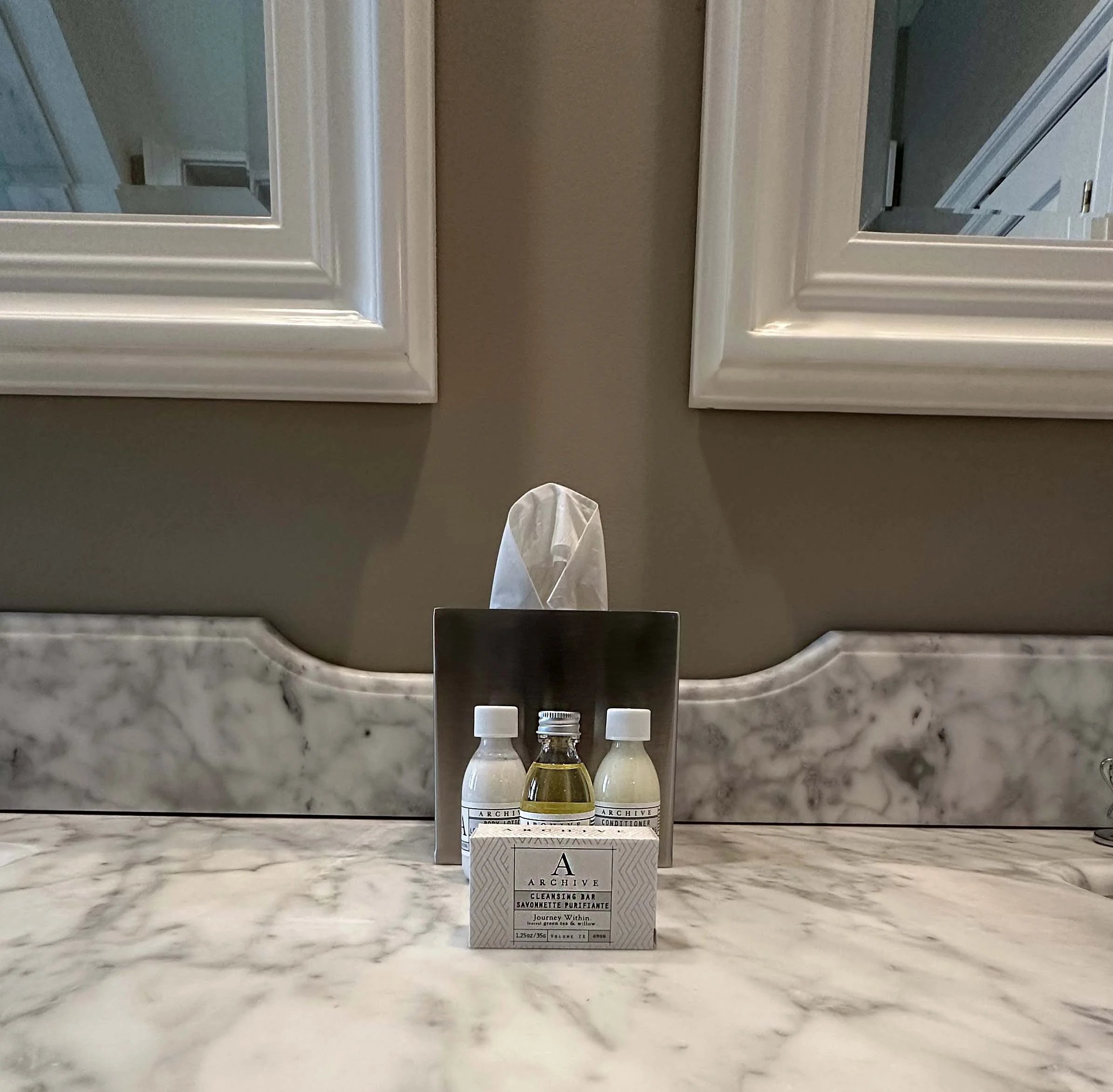 A marble bathroom vanity with a box of Archive products and a tissue box