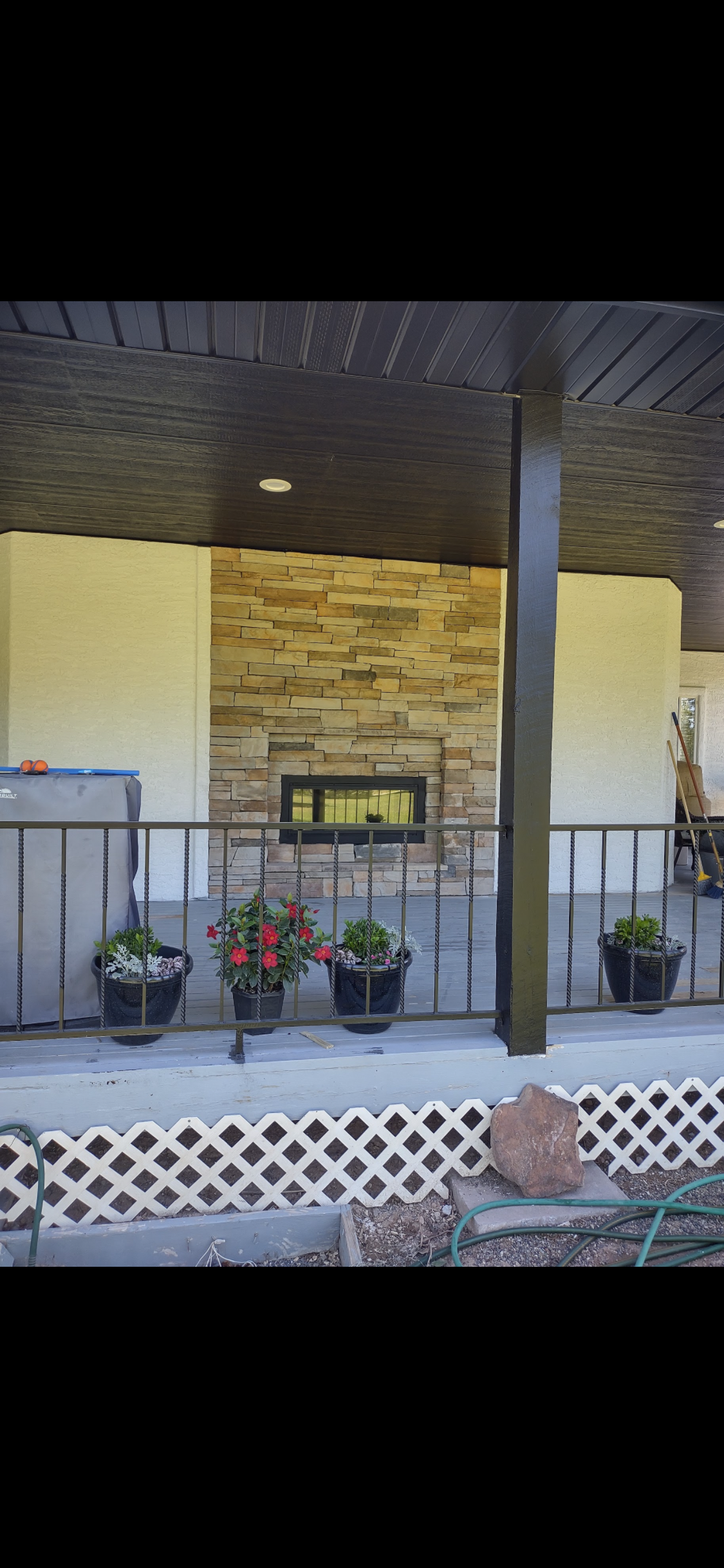 A covered patio with a stone fireplace, potted plants, and a metal railing