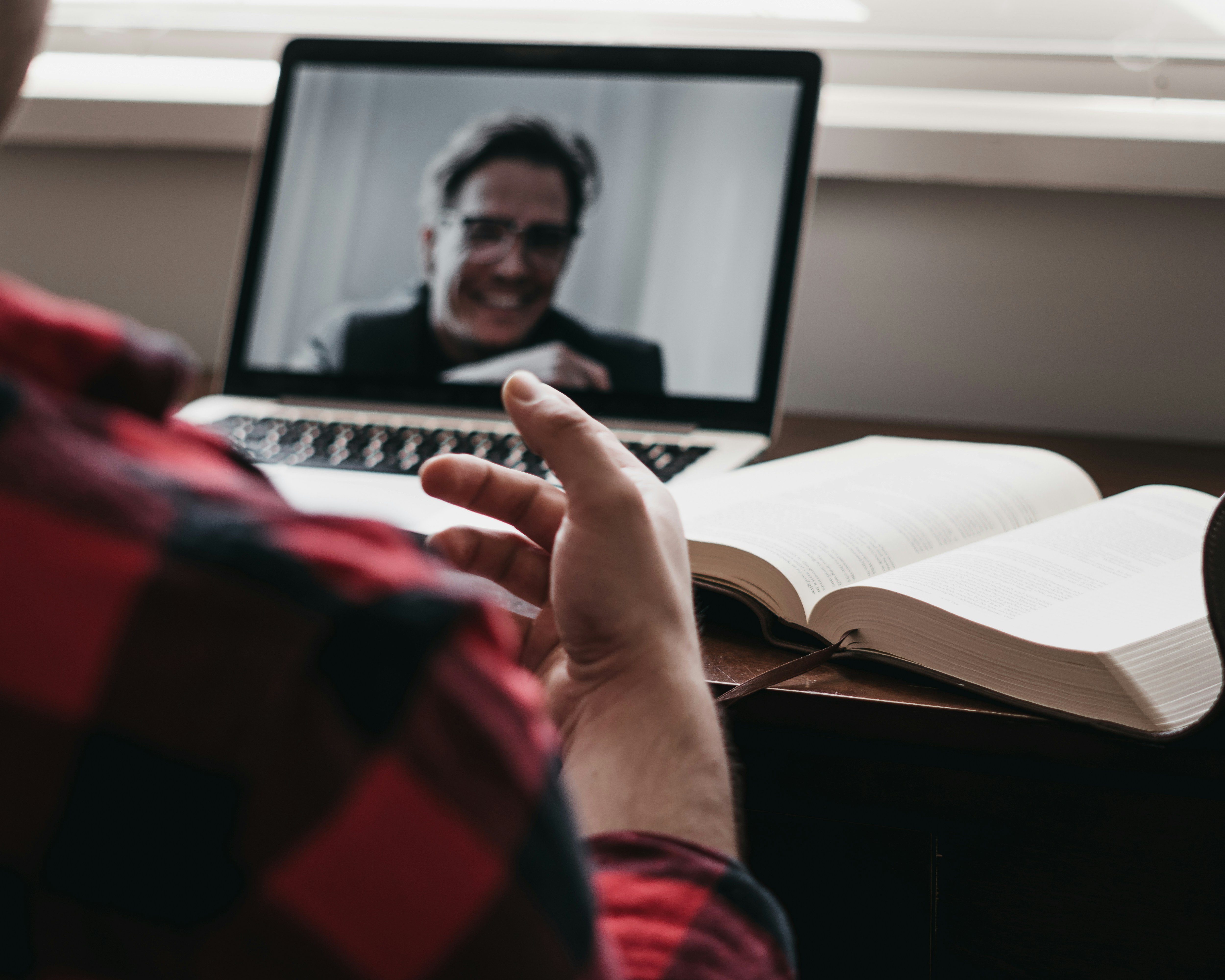 A person is sitting at a desk with a laptop, having a video call with another person.
