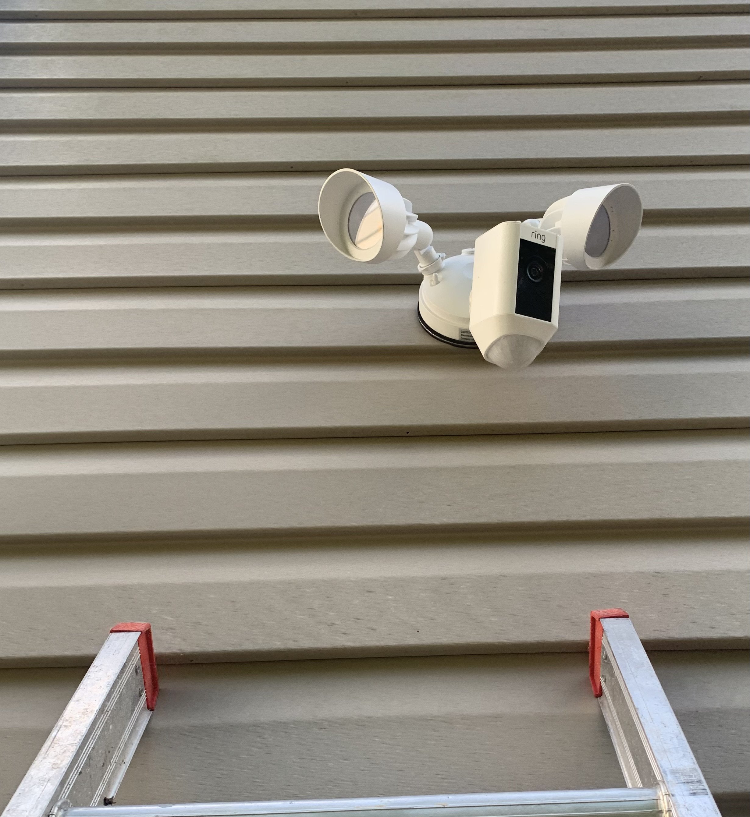 A white Ring security camera with lights mounted on a house's siding